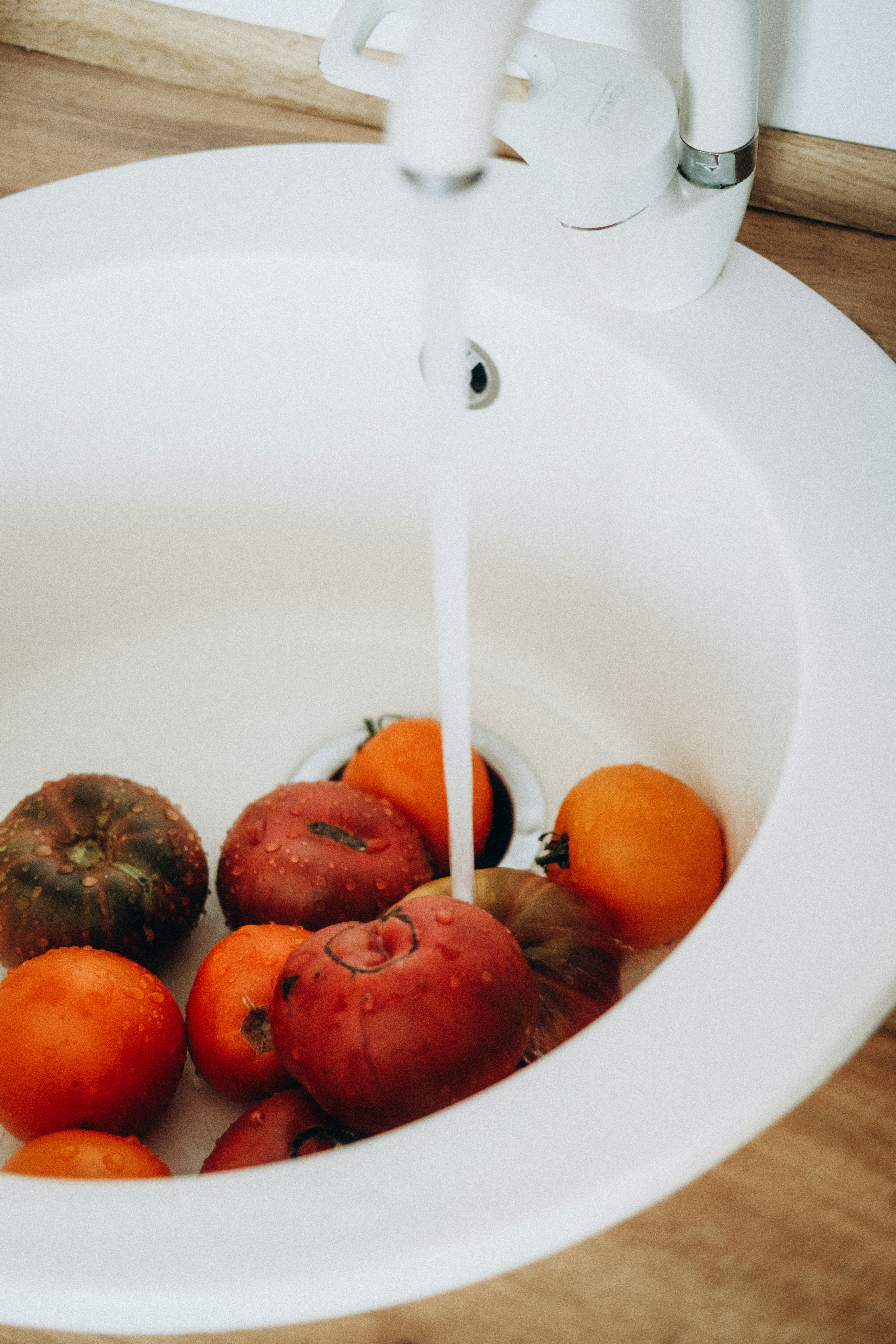Os tomates estão sendo lavados sob uma torneira aberta em uma pia.