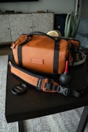 Brown camera bag with strap and blower on table.