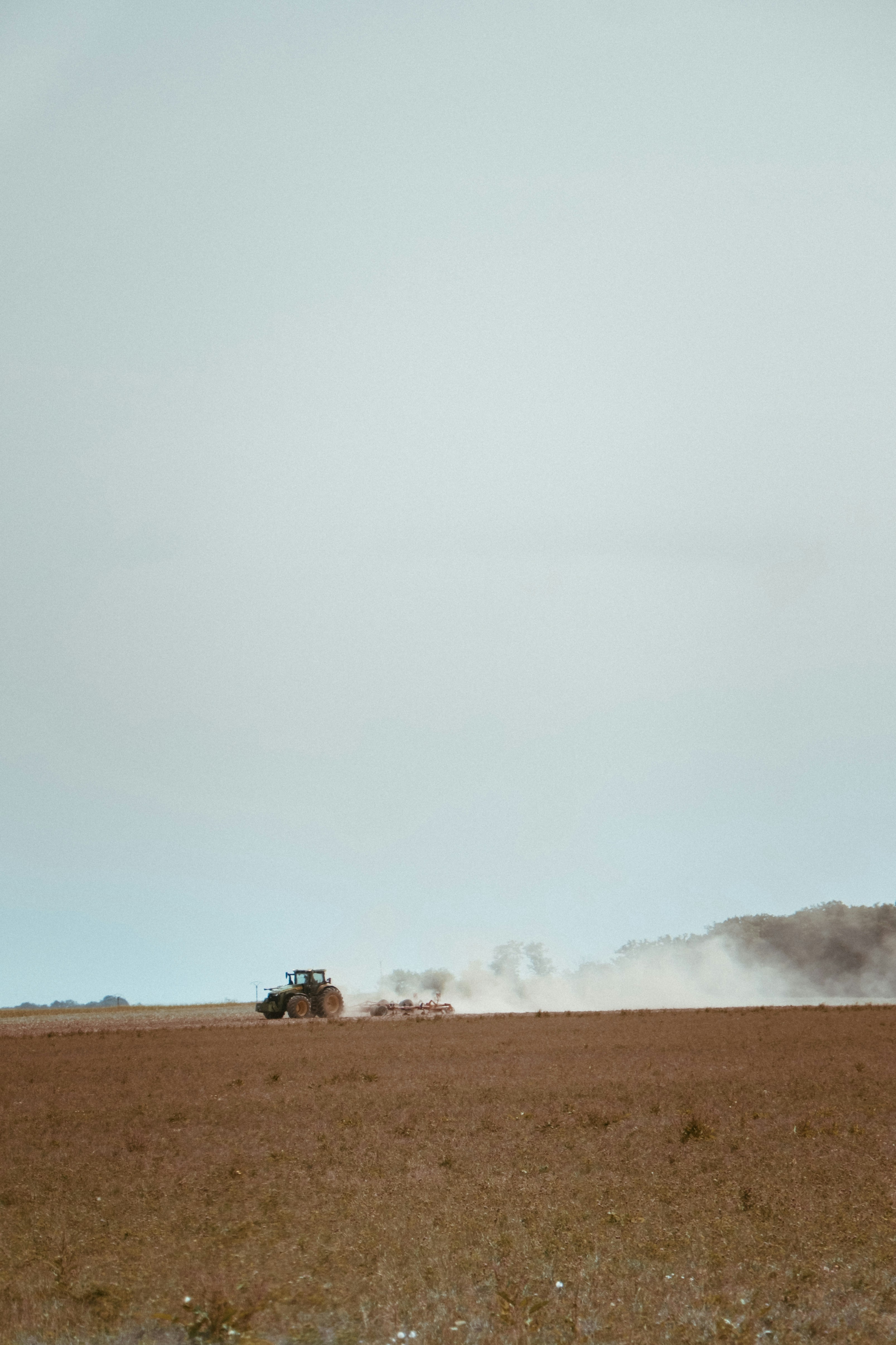 Tractor plowing a dry field under a hazy sky