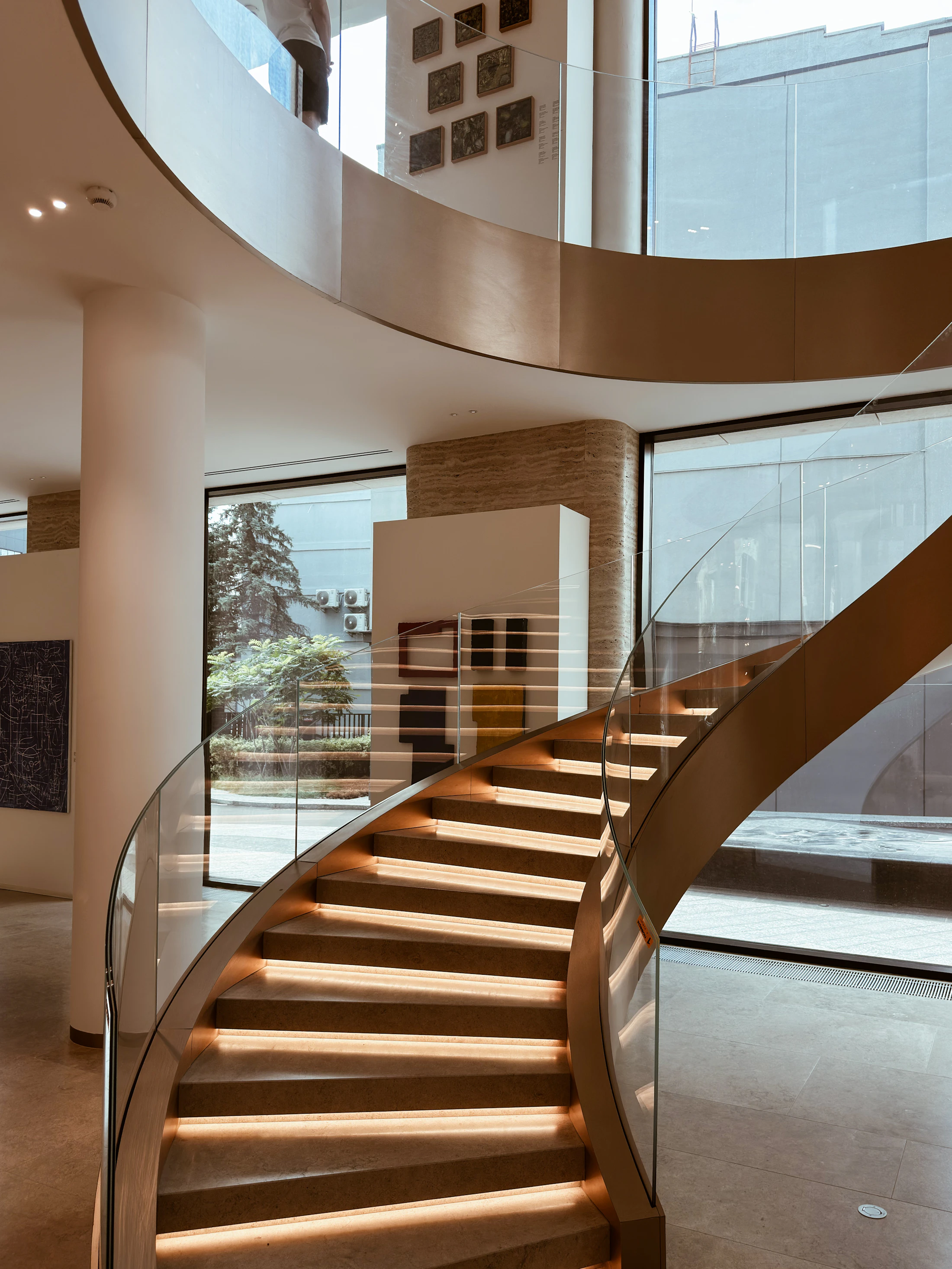 Modern curved wooden staircase with glass railing and lighting