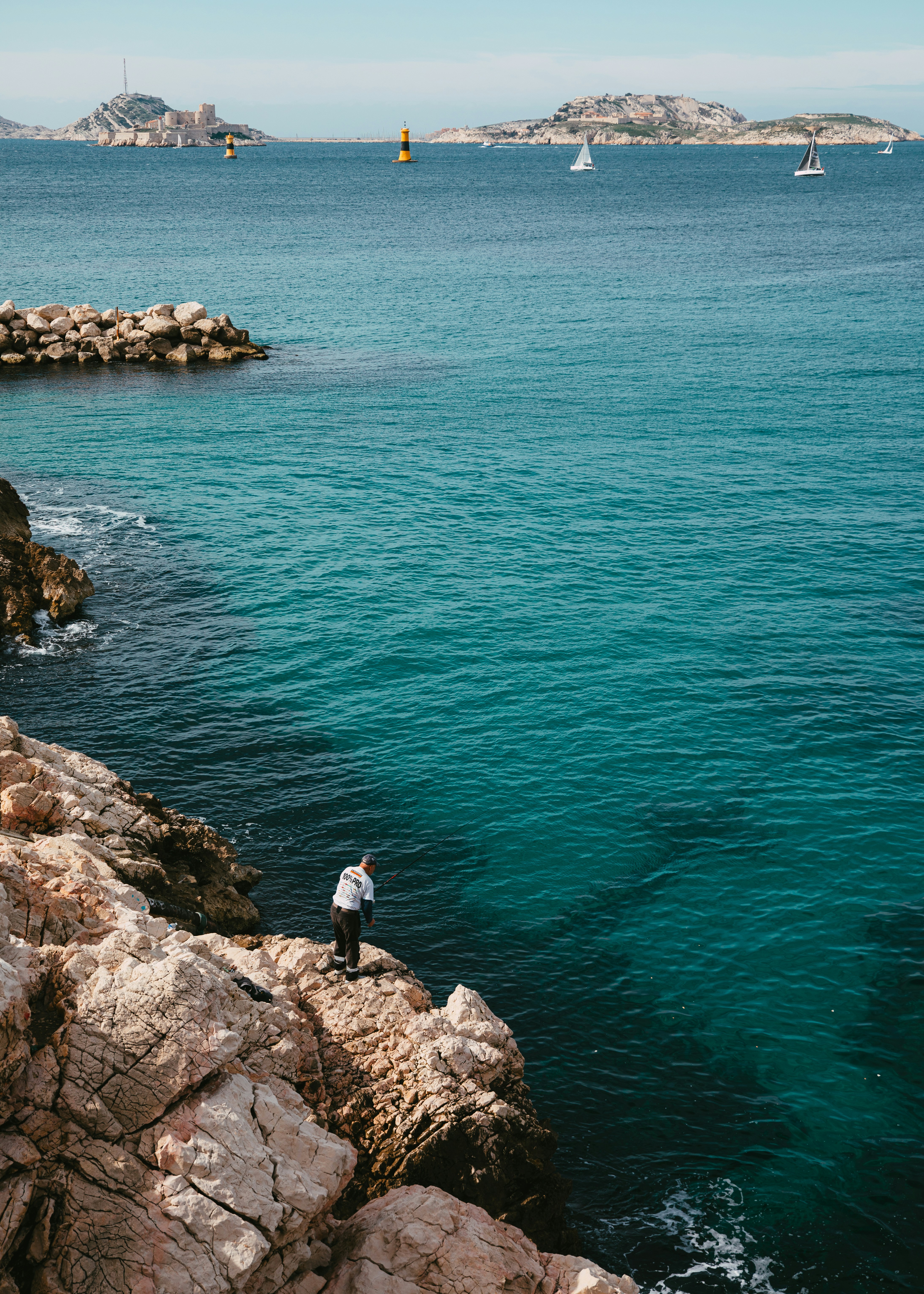 Hombre pescando desde la costa rocosa con vistas al océano azul