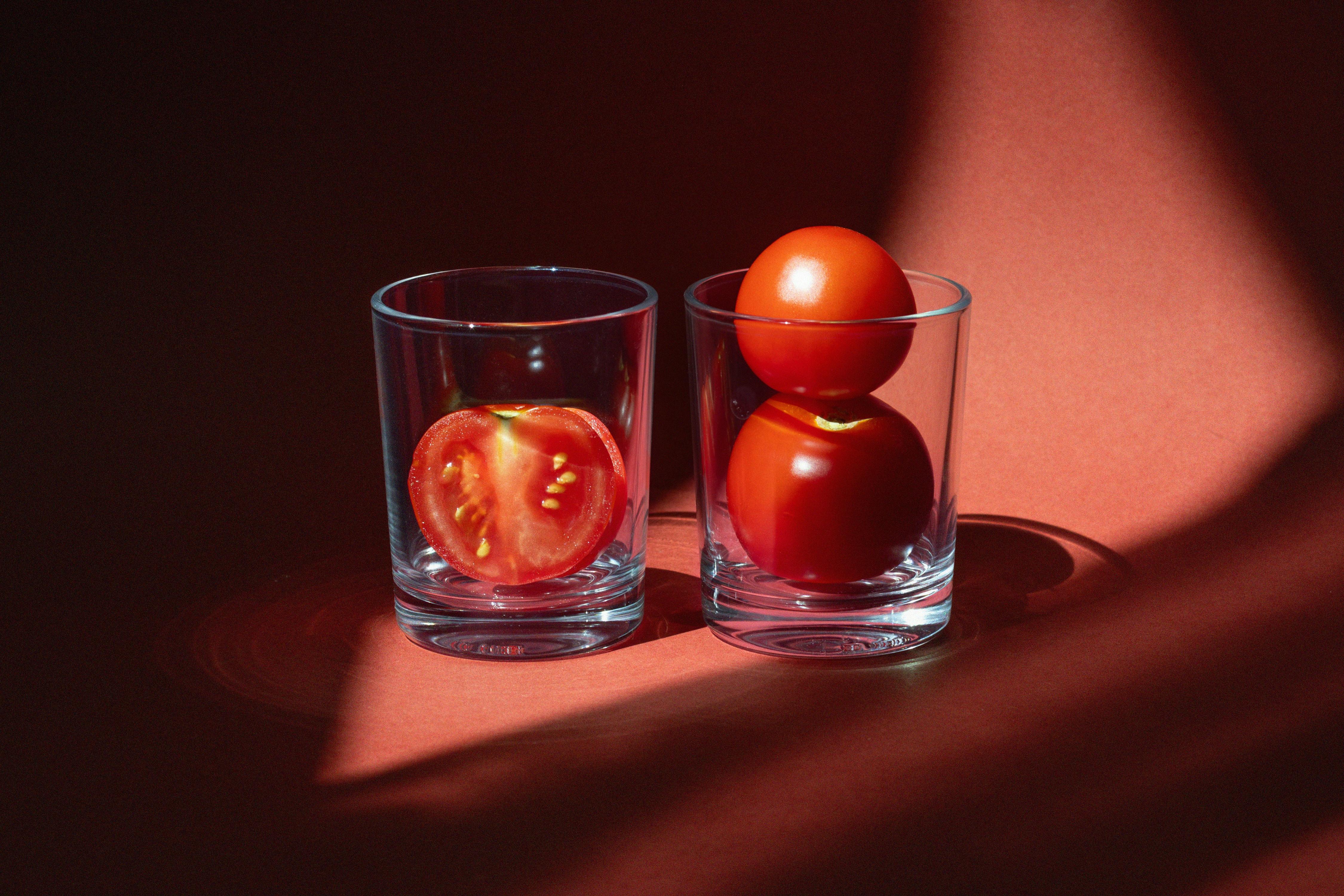 Deux verres avec des tomates sur une surface rouge.