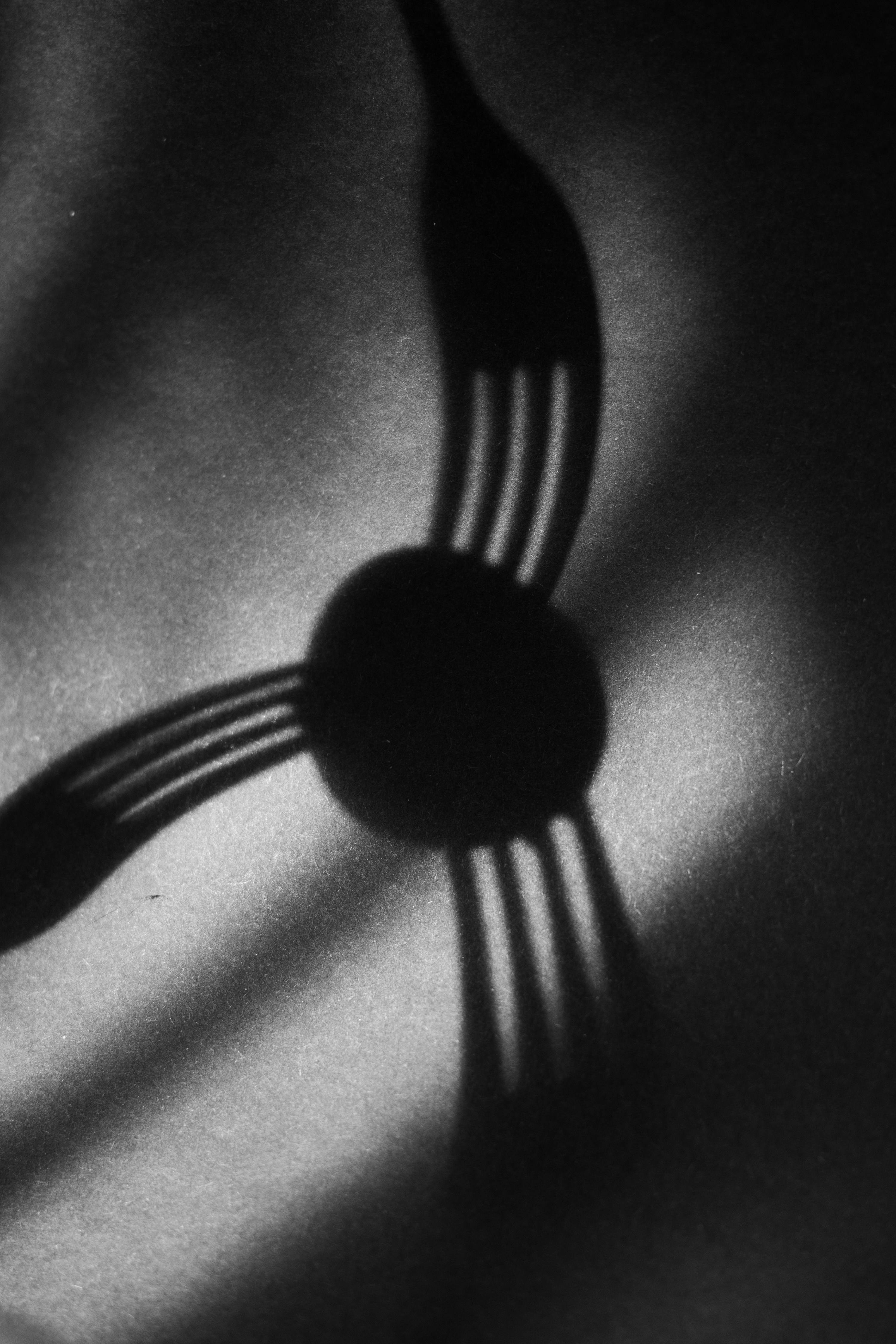 Trois fourchettes projetant des ombres autour d’un objet central.