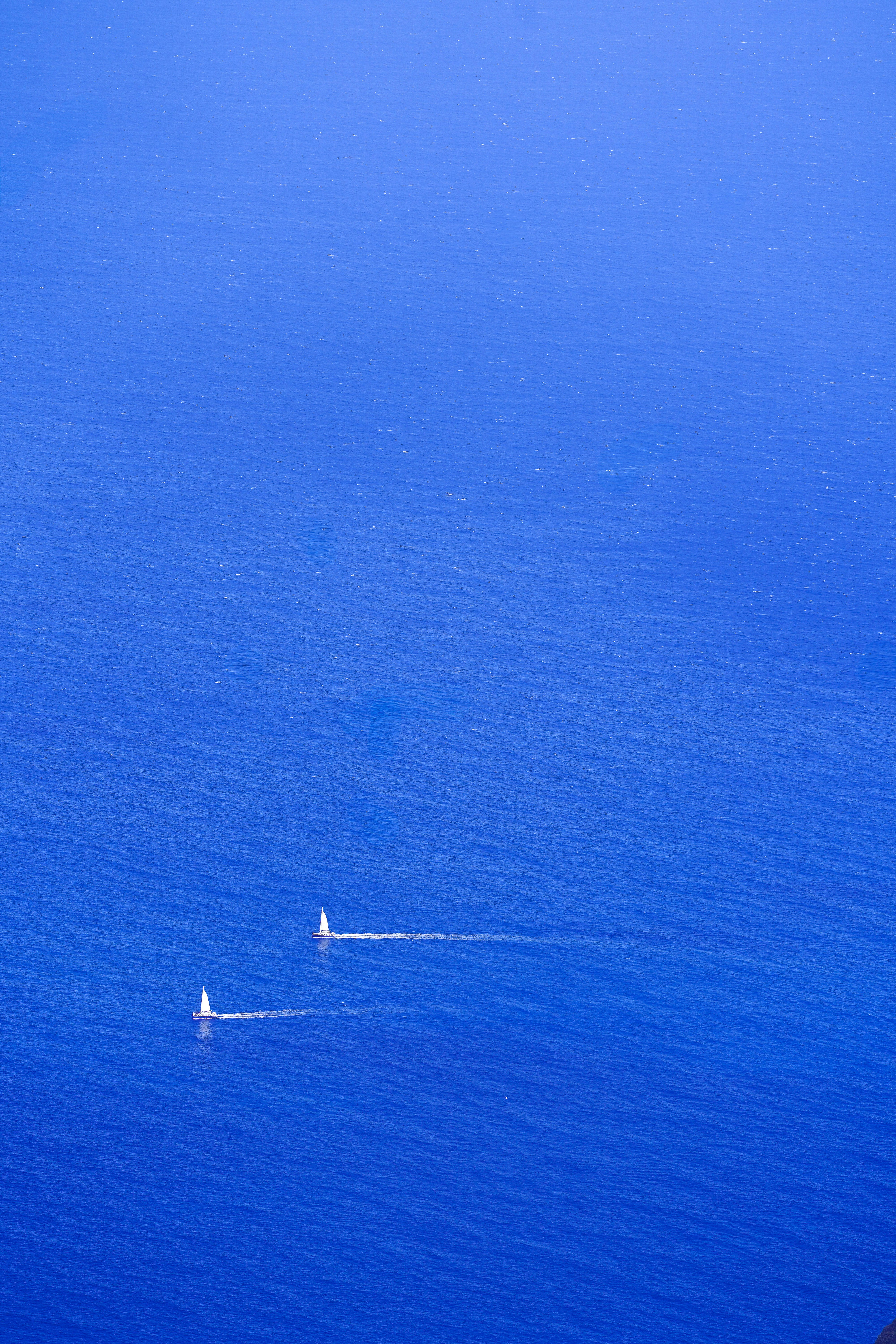 Two sailboats glide across a vast blue ocean.
