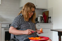 Woman in wheelchair peeling vegetables in kitchen.