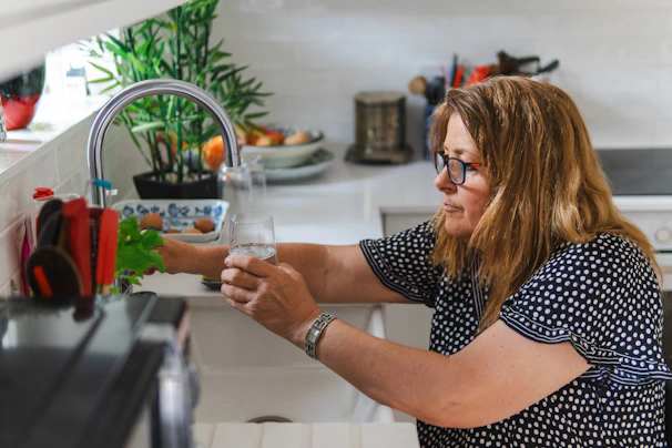 Woman filling a glass with water from a kitchen faucet