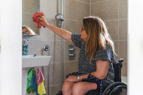 Woman in wheelchair cleaning bathroom mirror