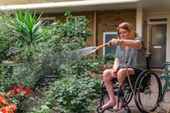 Woman in wheelchair waters plants in garden.