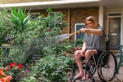 Woman in wheelchair waters plants in garden.