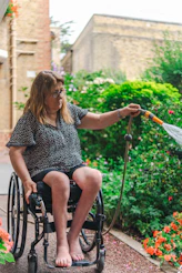 Woman in wheelchair watering plants in garden.