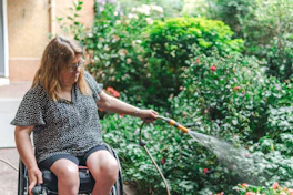 Woman in wheelchair waters plants with hose