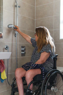 Woman in wheelchair using shower head in accessible bathroom