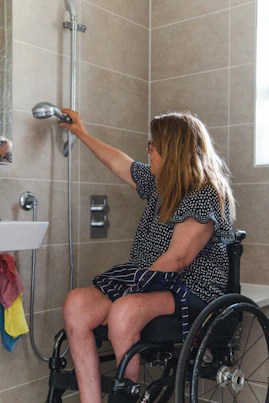 Woman in wheelchair using shower head in accessible bathroom