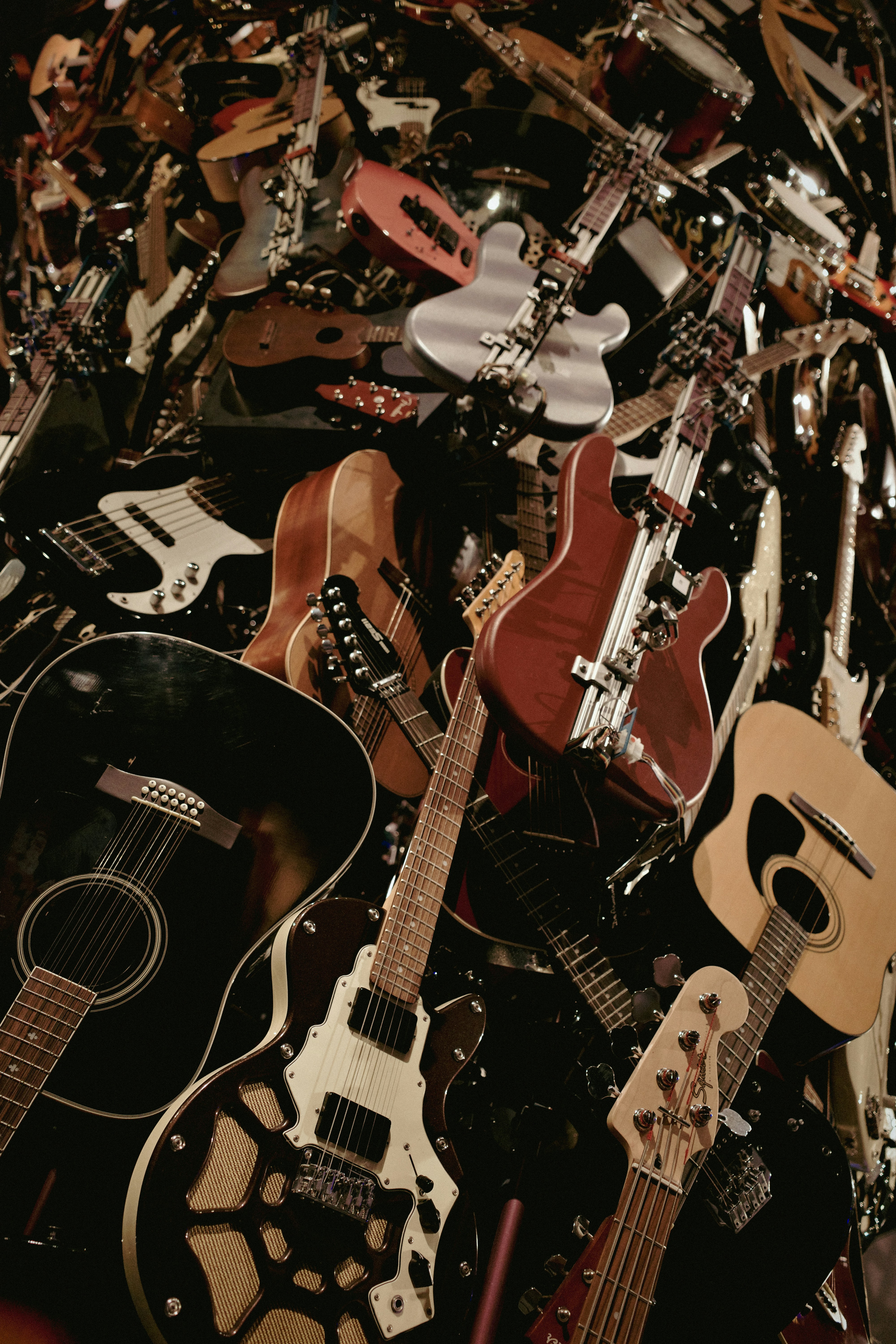 A large pile of various guitars and guitar parts.