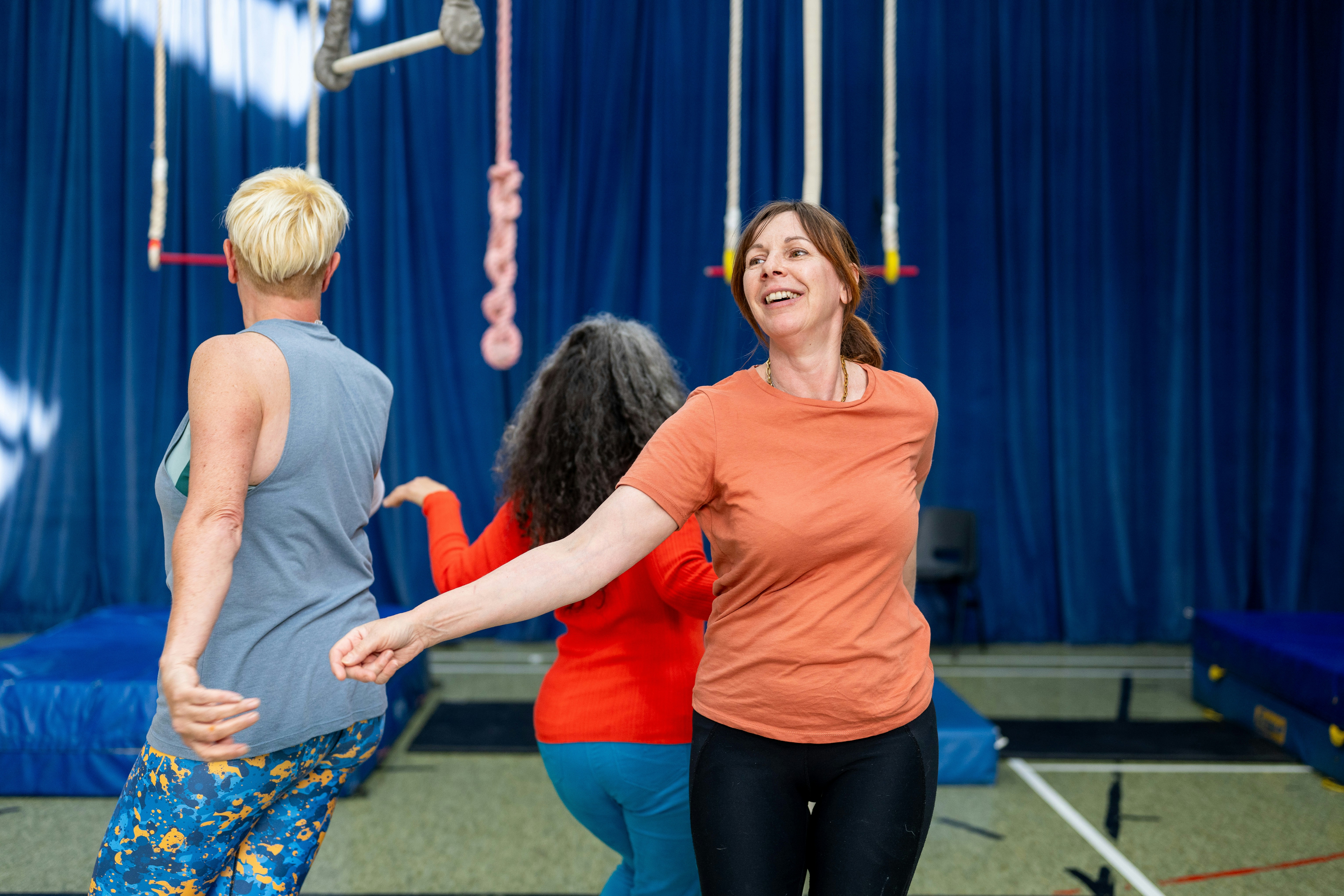 Three people dancing in a studio with blue curtains