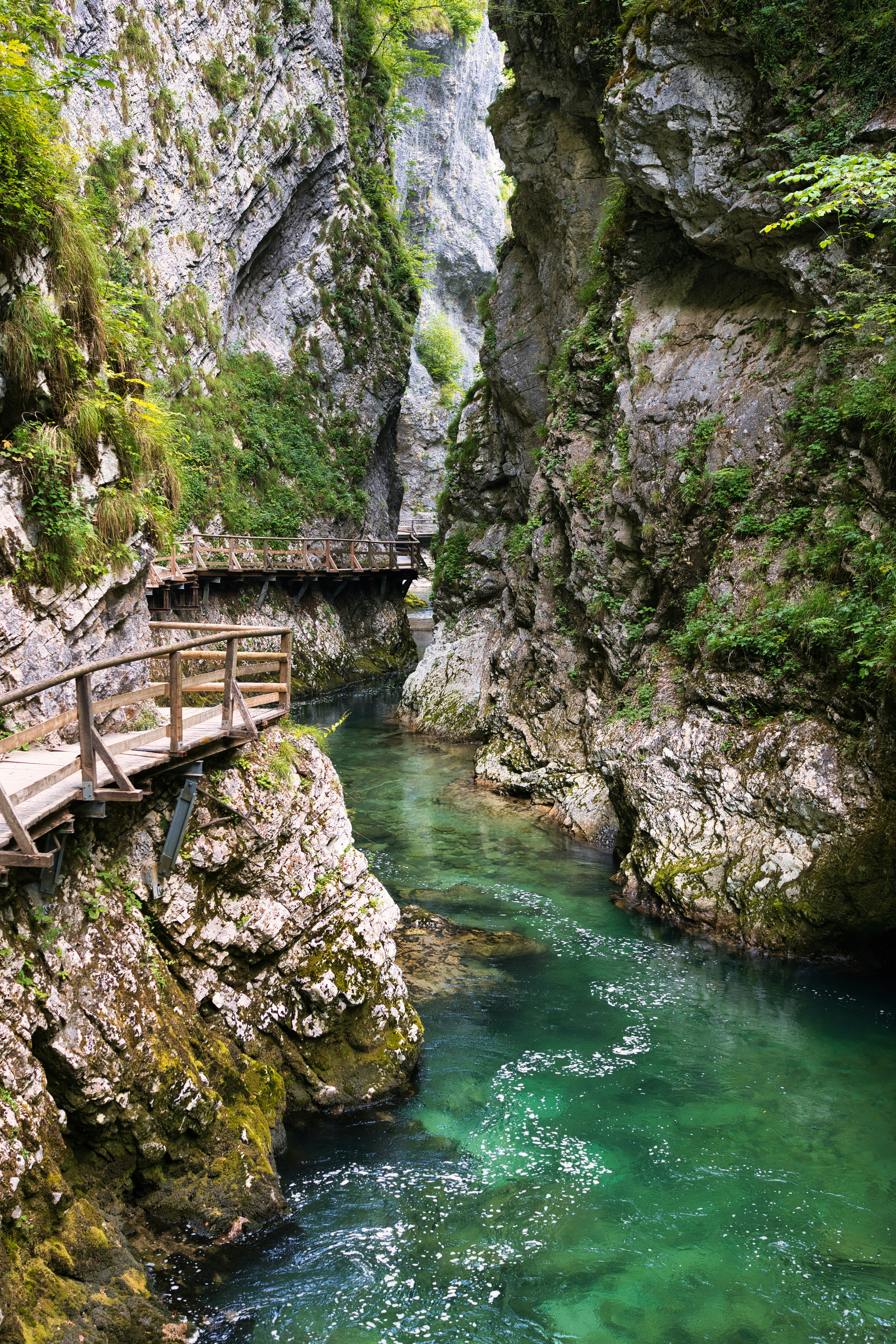Wooden walkway along a clear river in a rocky gorge.