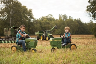 Two boys riding pedal tractors in a field