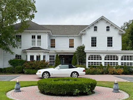 White convertible parked in front of a large white house.