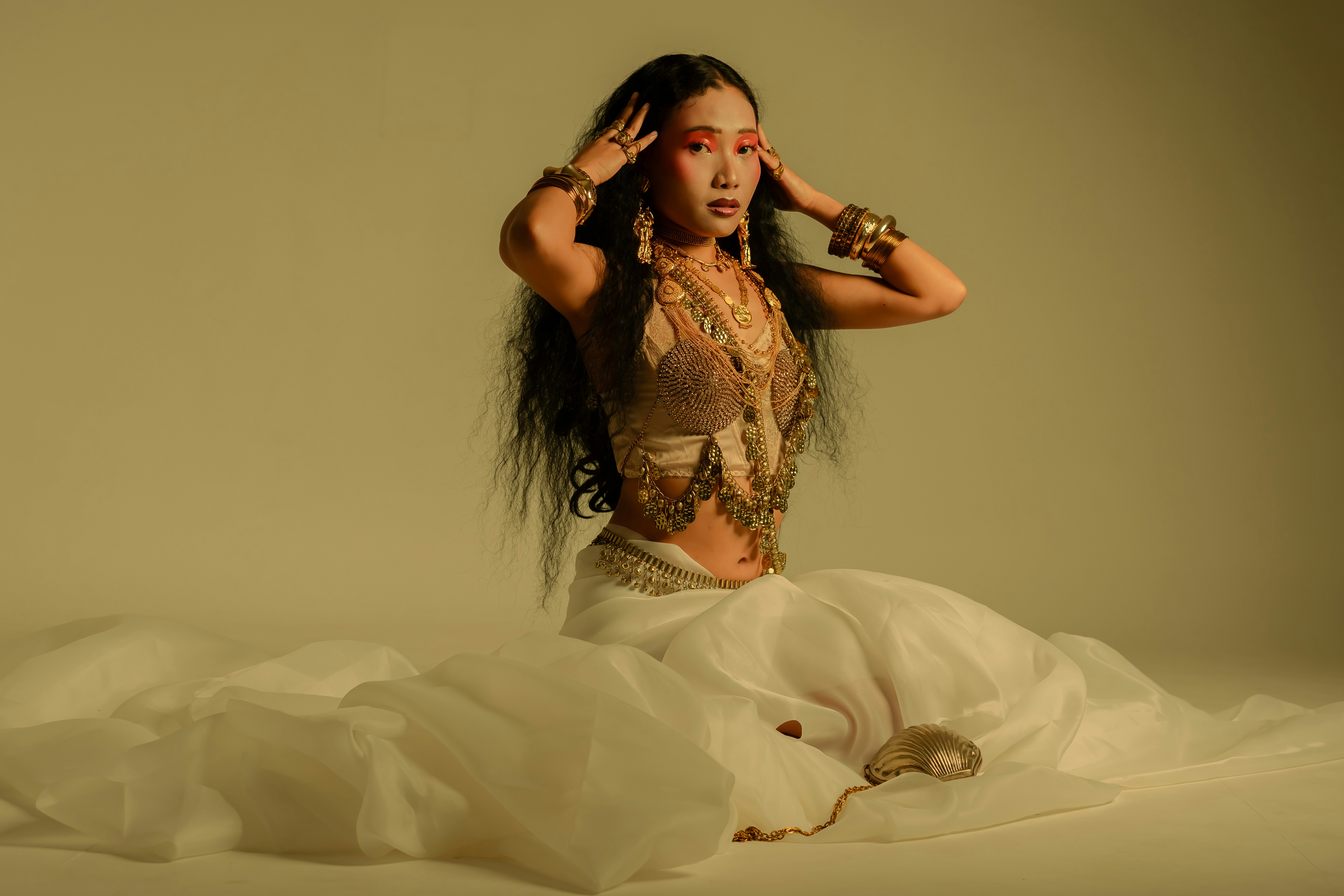 A striking editorial portrait of a female model styled in gold jewelry and cultural fashion. The image blends modern muse aesthetics with traditional ethnic elegance, captured in a creative test shoot.