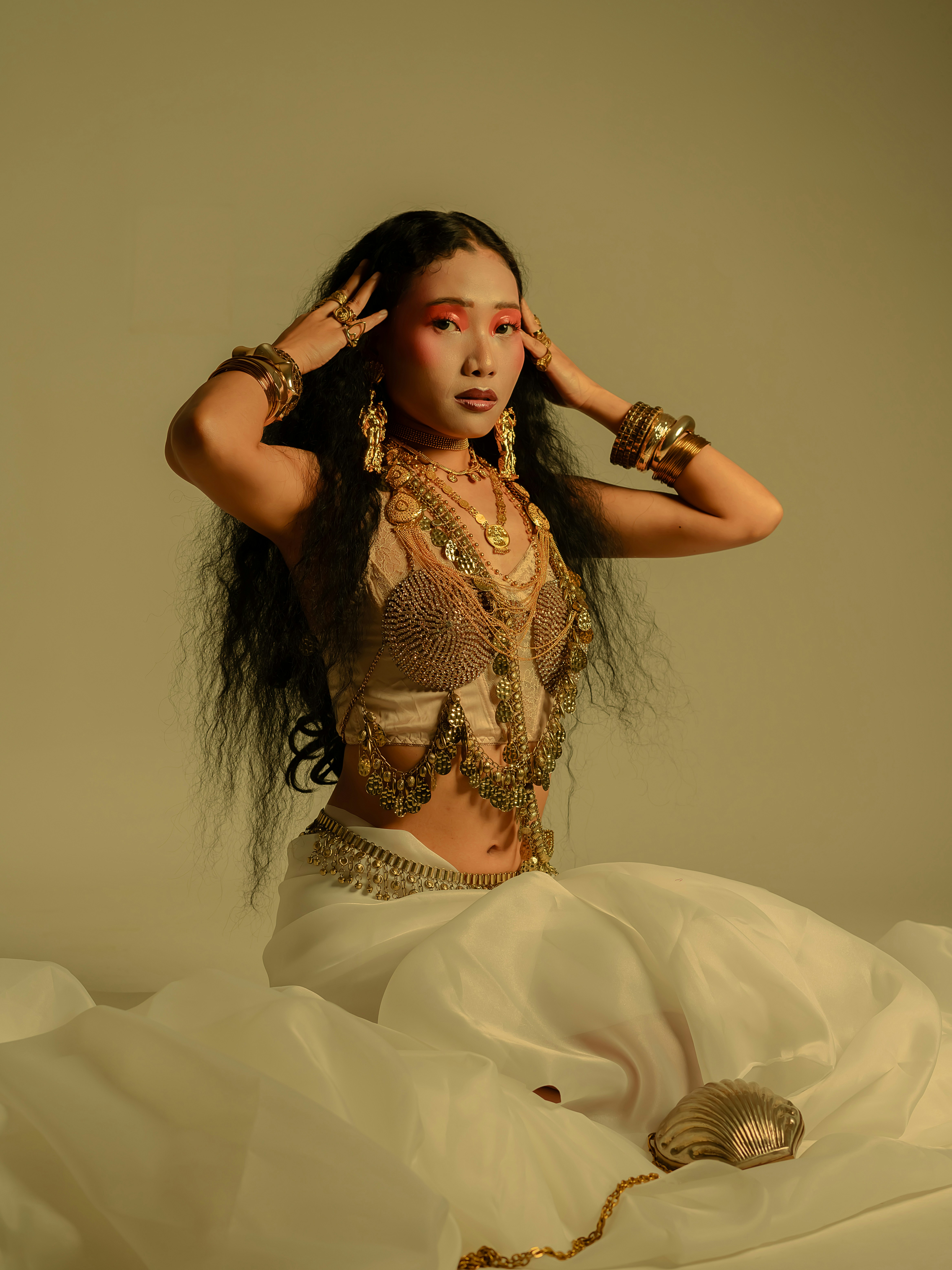 Woman in ornate jewelry and white skirt poses