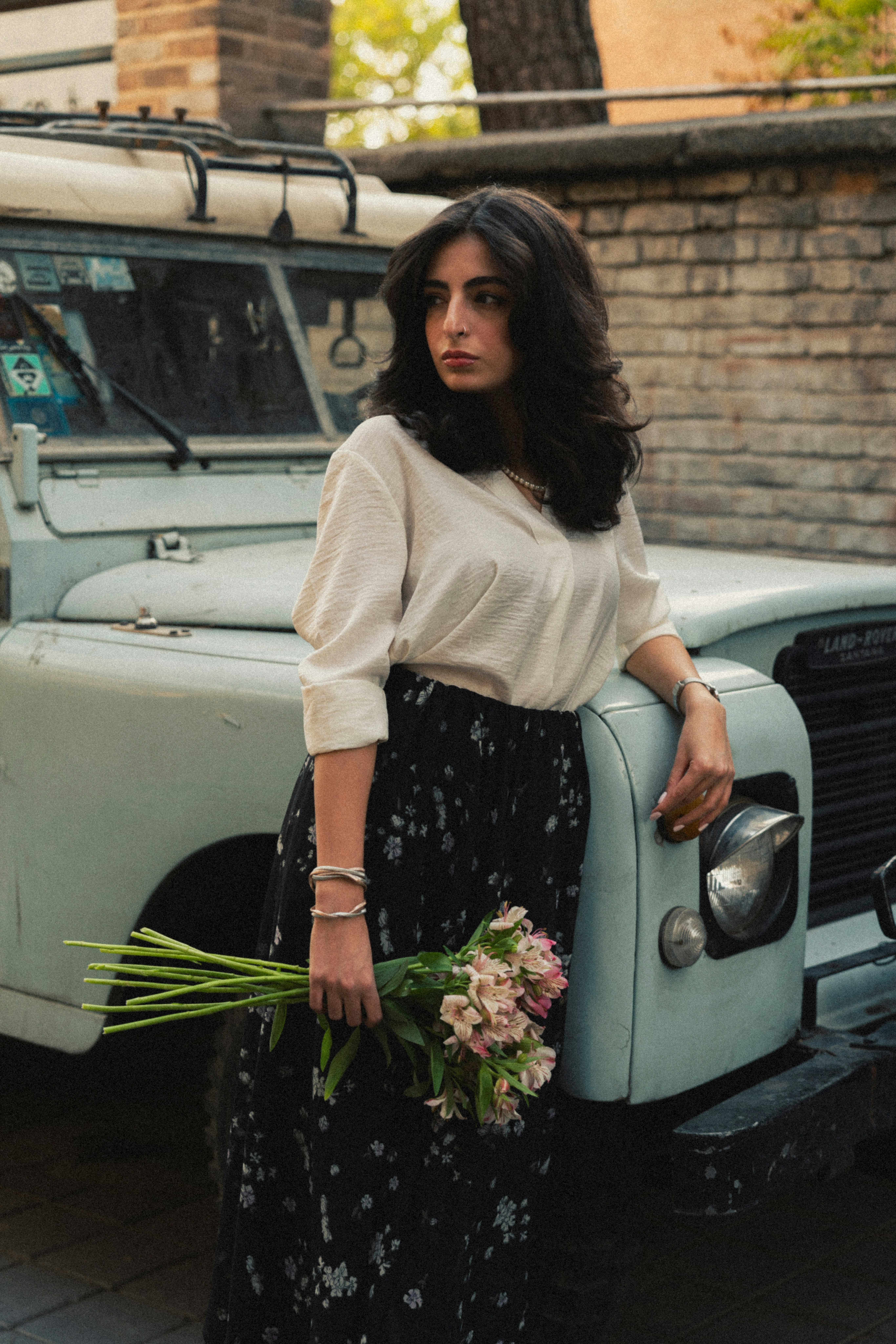 Woman holding flowers leans on vintage vehicle