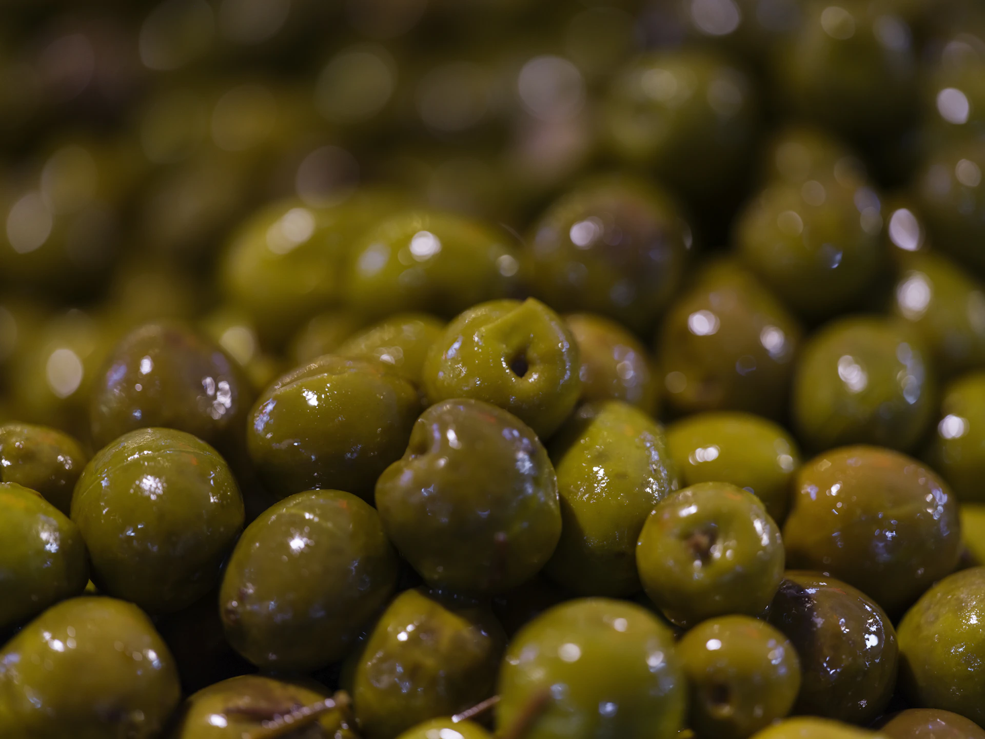 Pile of glossy green olives with pits
