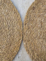 Two woven round placemats on a textured surface