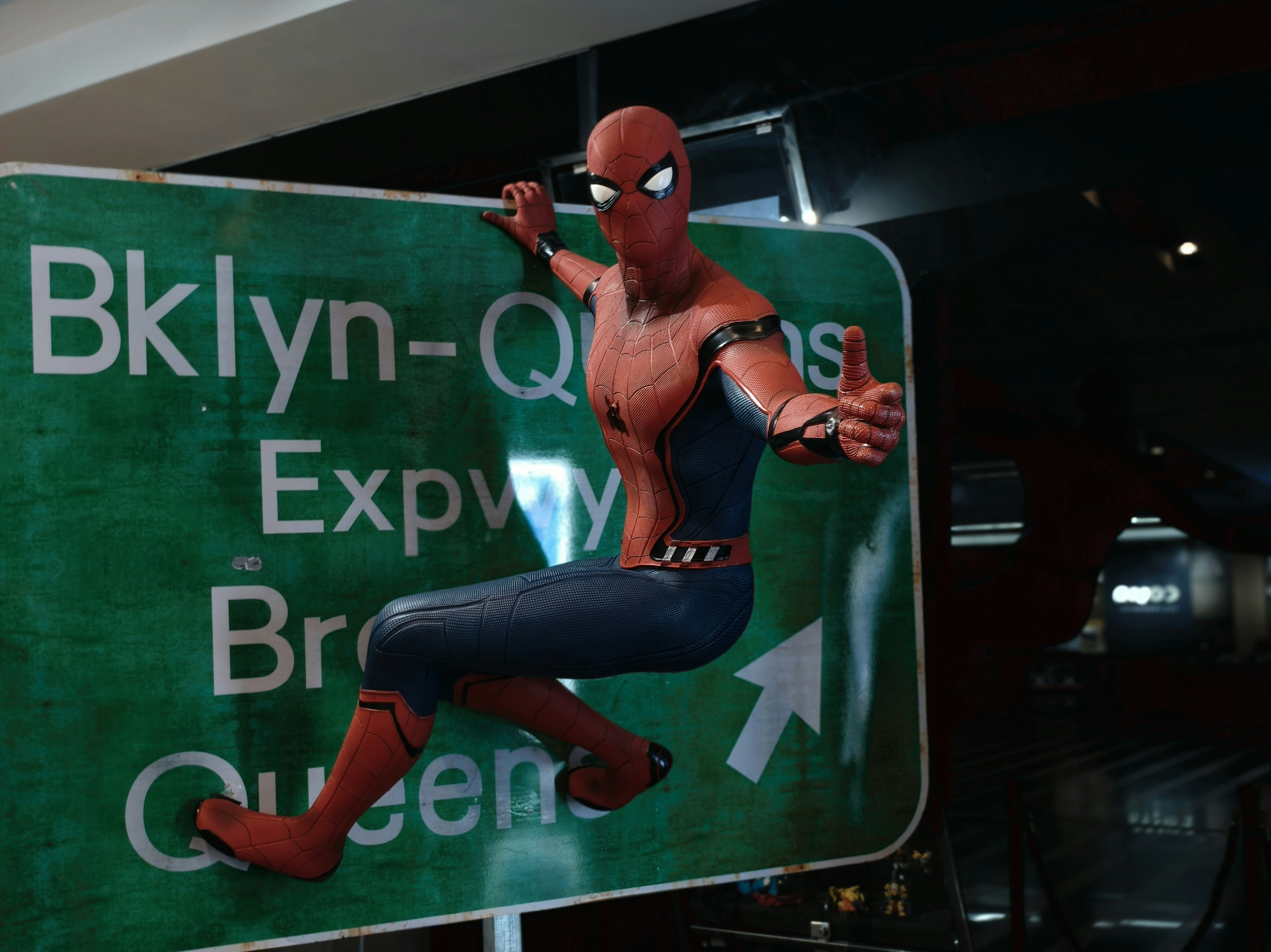 Spider-man sits on a brooklyn-queens expressway sign.