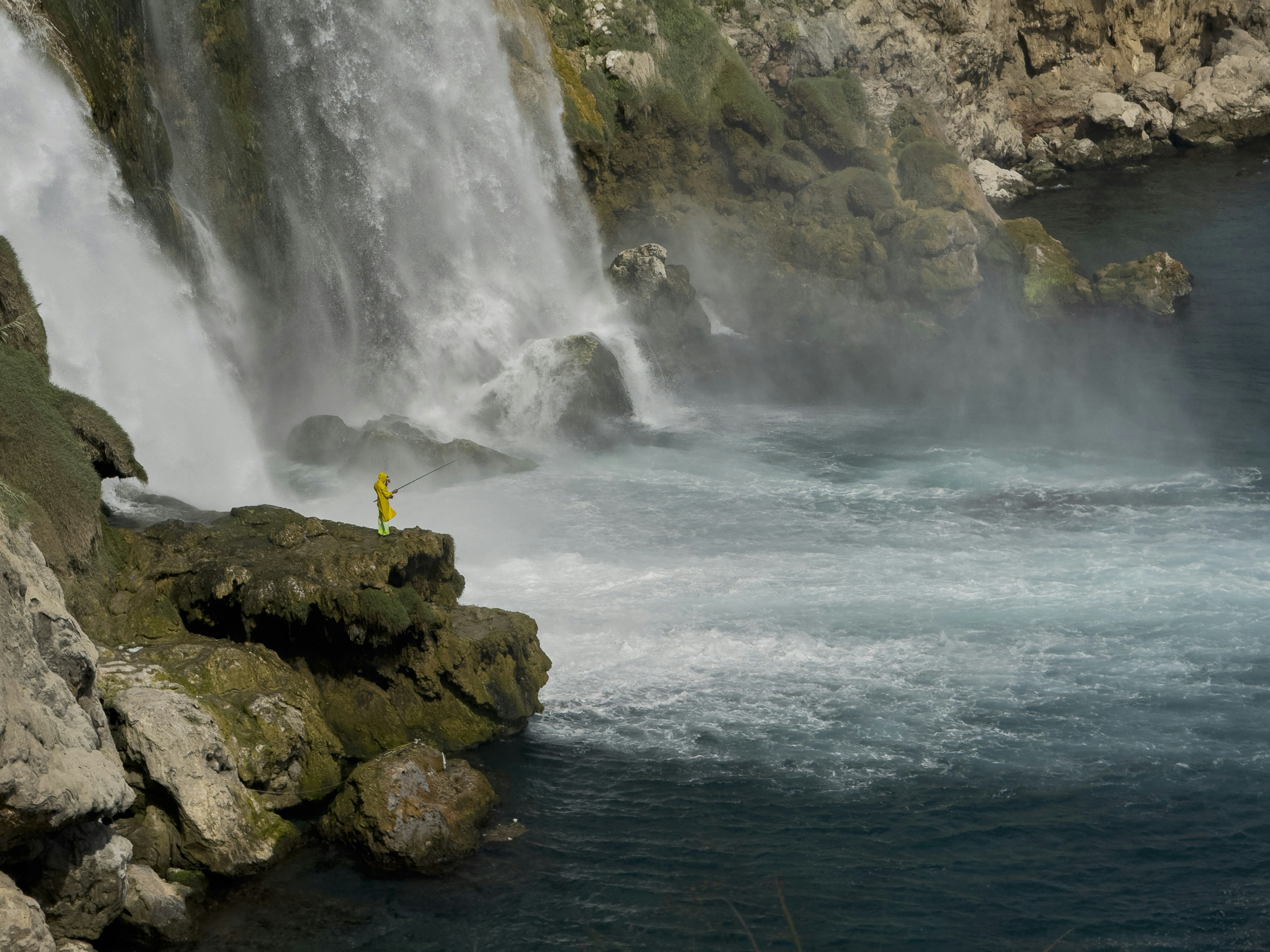 A person stands near a large waterfall cascading into the ocean. 풍경 사진