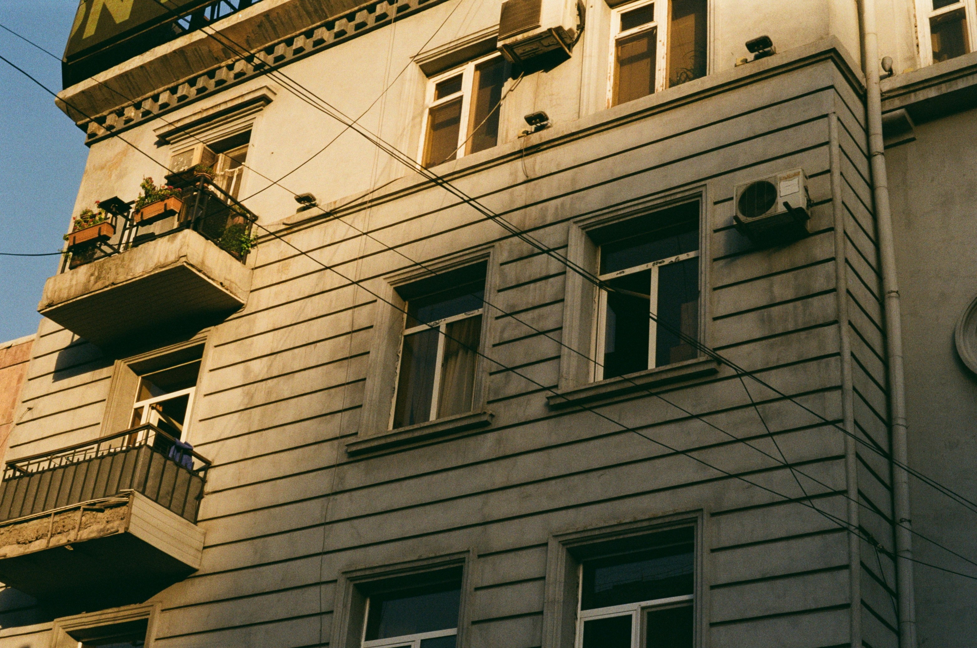 A weathered building exterior featuring multiple windows and a balcony adorned with plants, capturing the essence of urban living.
