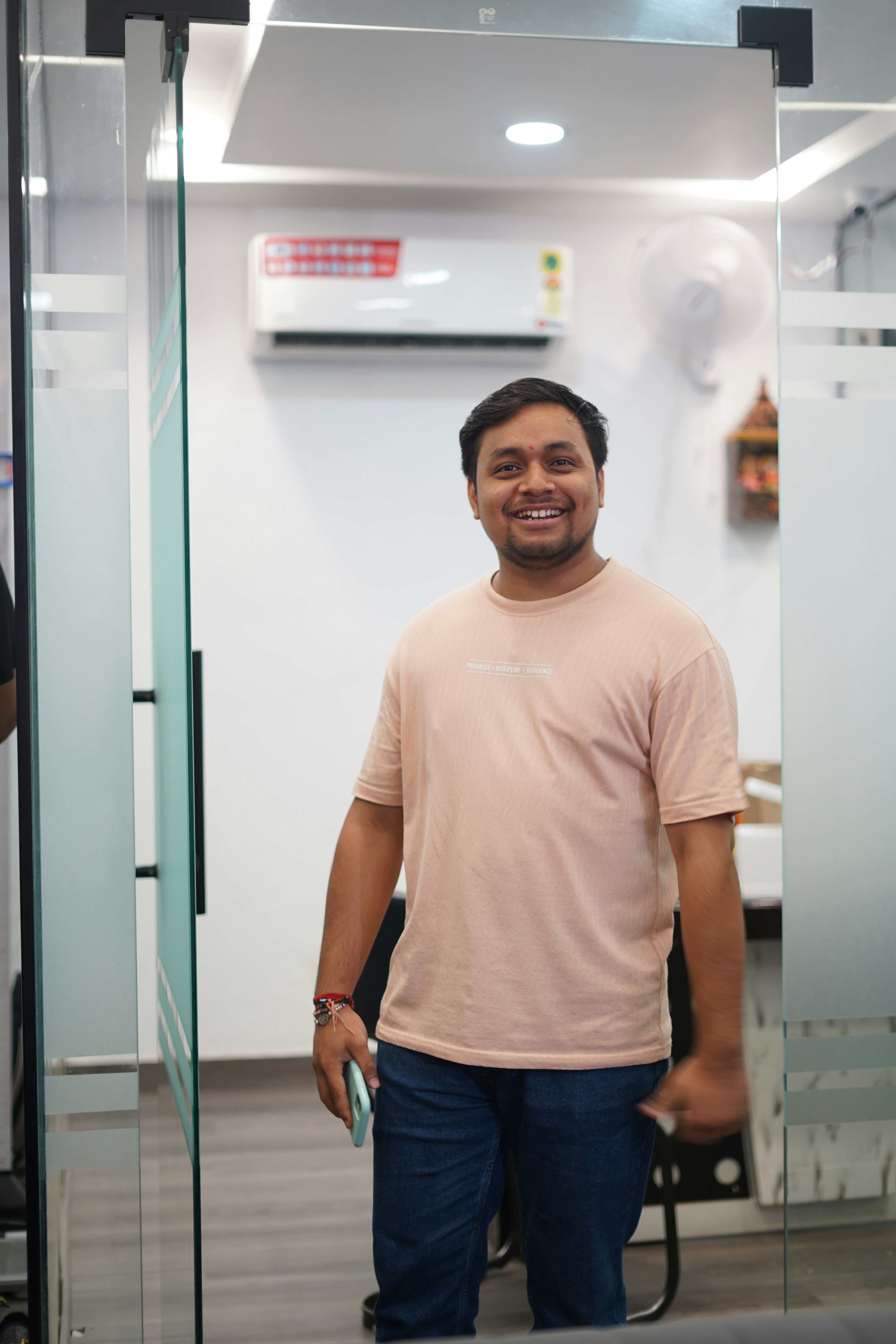 Hombre sonriente sostiene un smartphone en el umbral de una oficina.