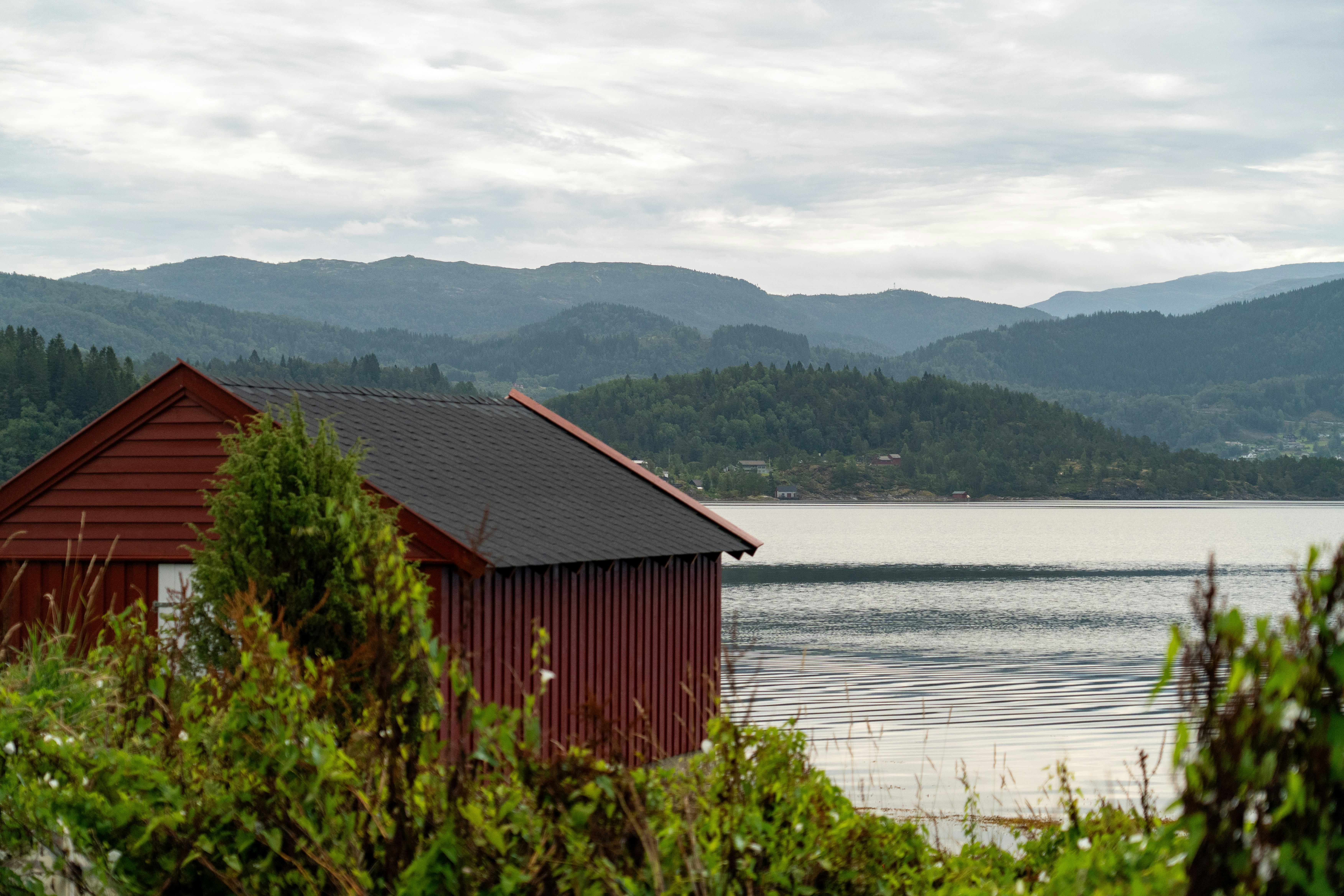 Red boathouse on a lake with rolling hills.