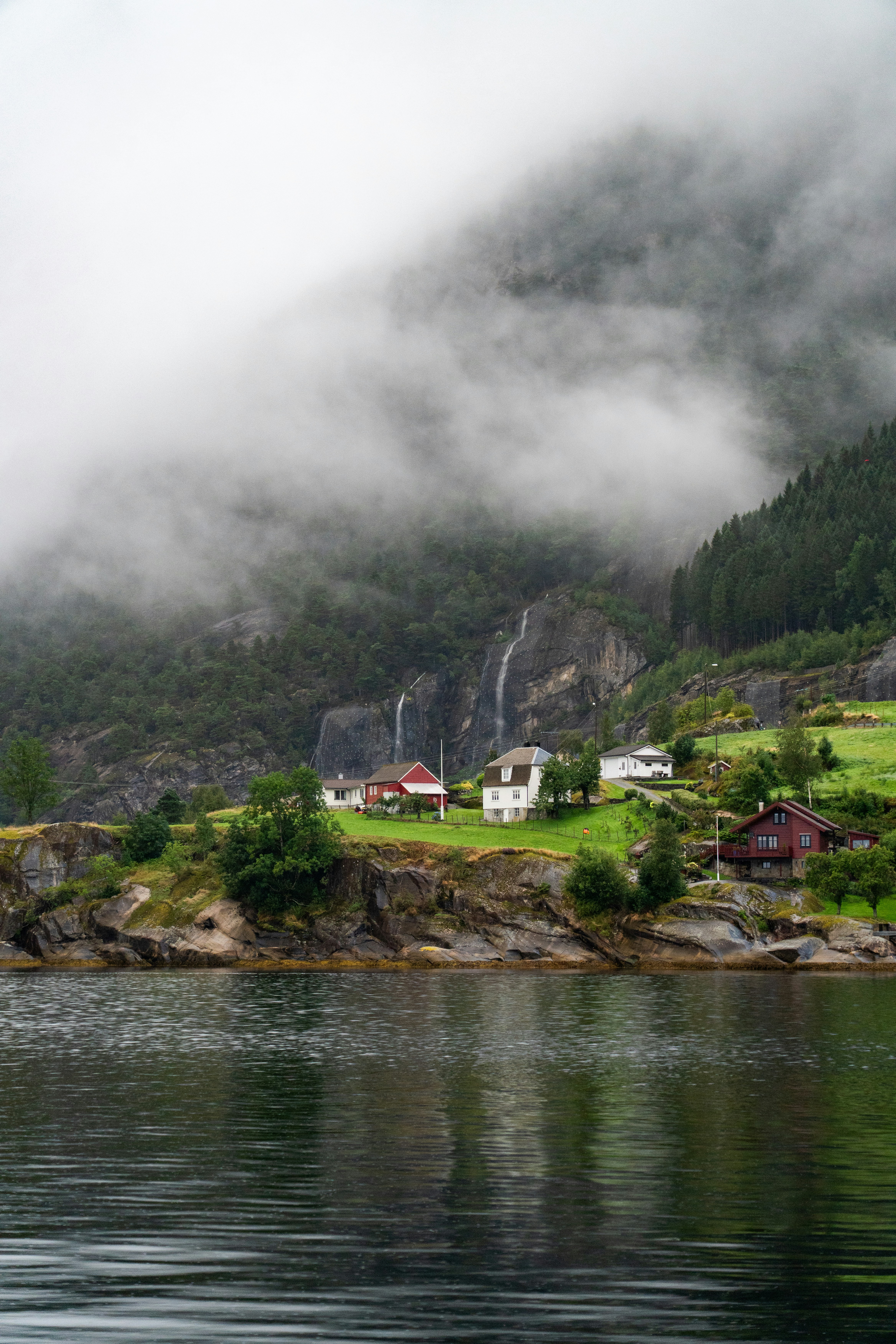 Small village nestled by a misty fjord with waterfalls.