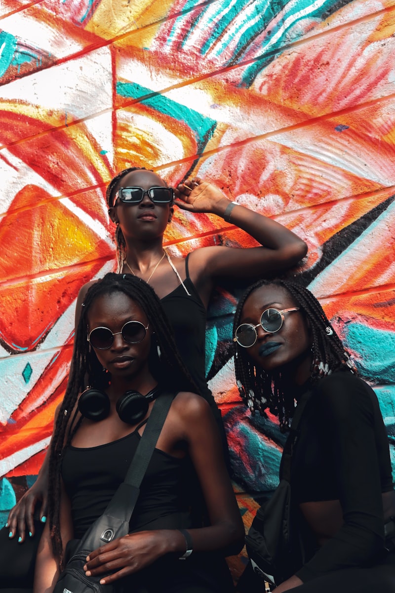 Three Black women friends posing together in front of a vibrant colorful mural