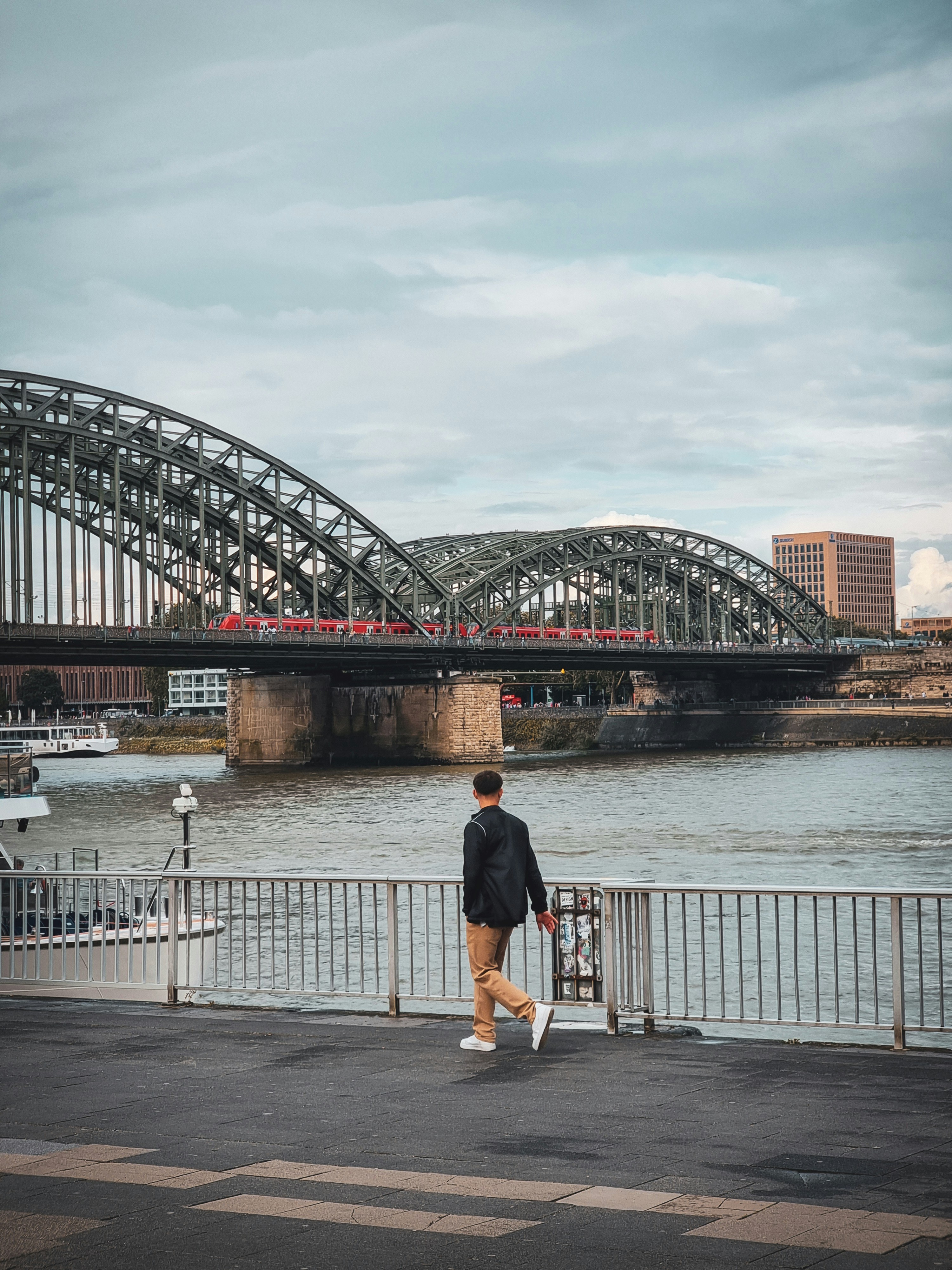 Man walks by river with large arched bridge in background