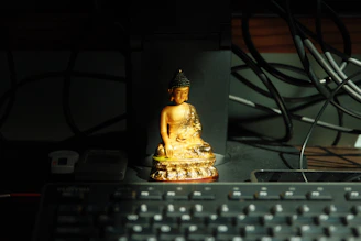 Golden buddha statue on a desk with keyboard.
