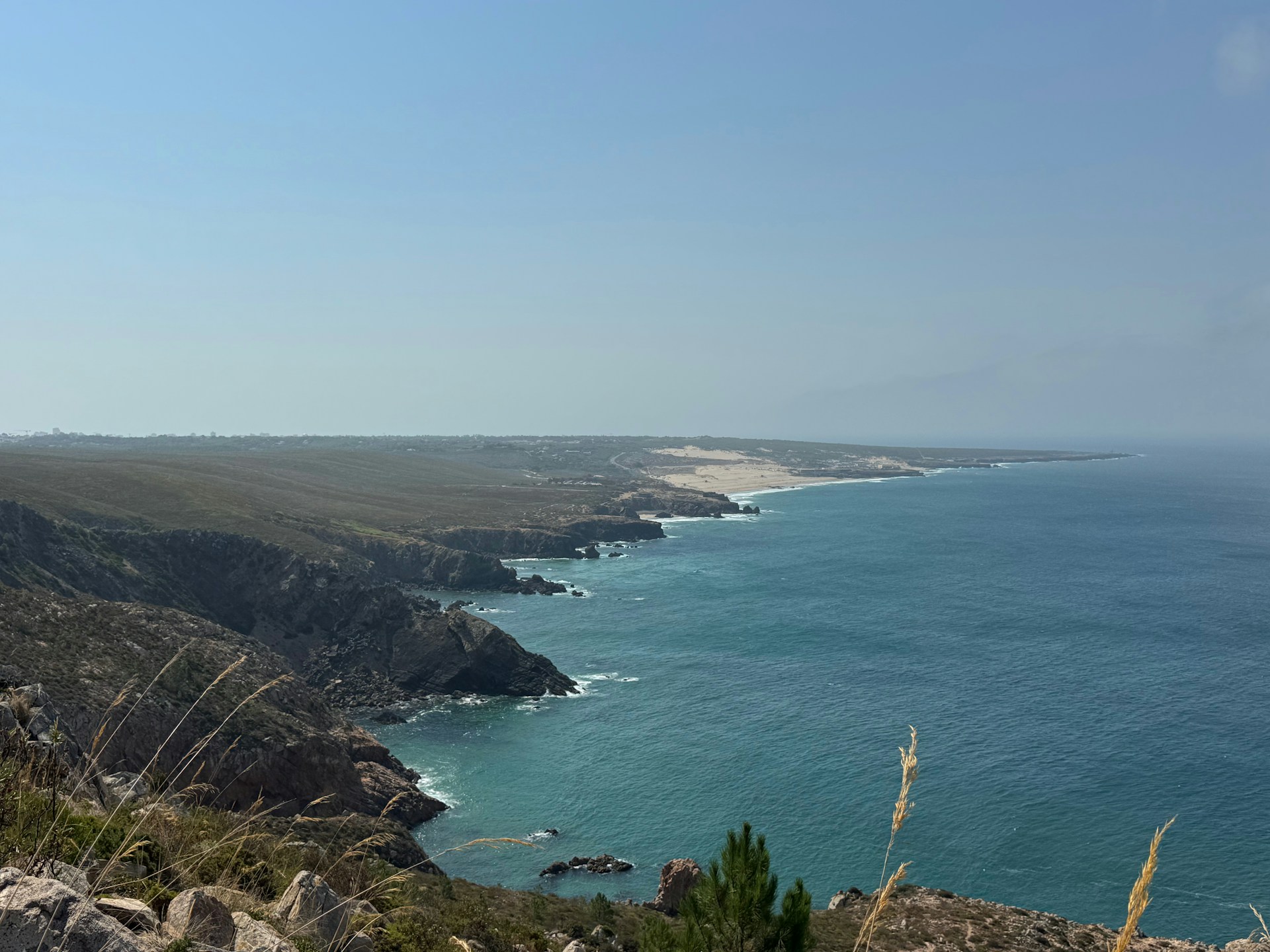 Coastal cliffs meet the blue ocean under a clear sky.