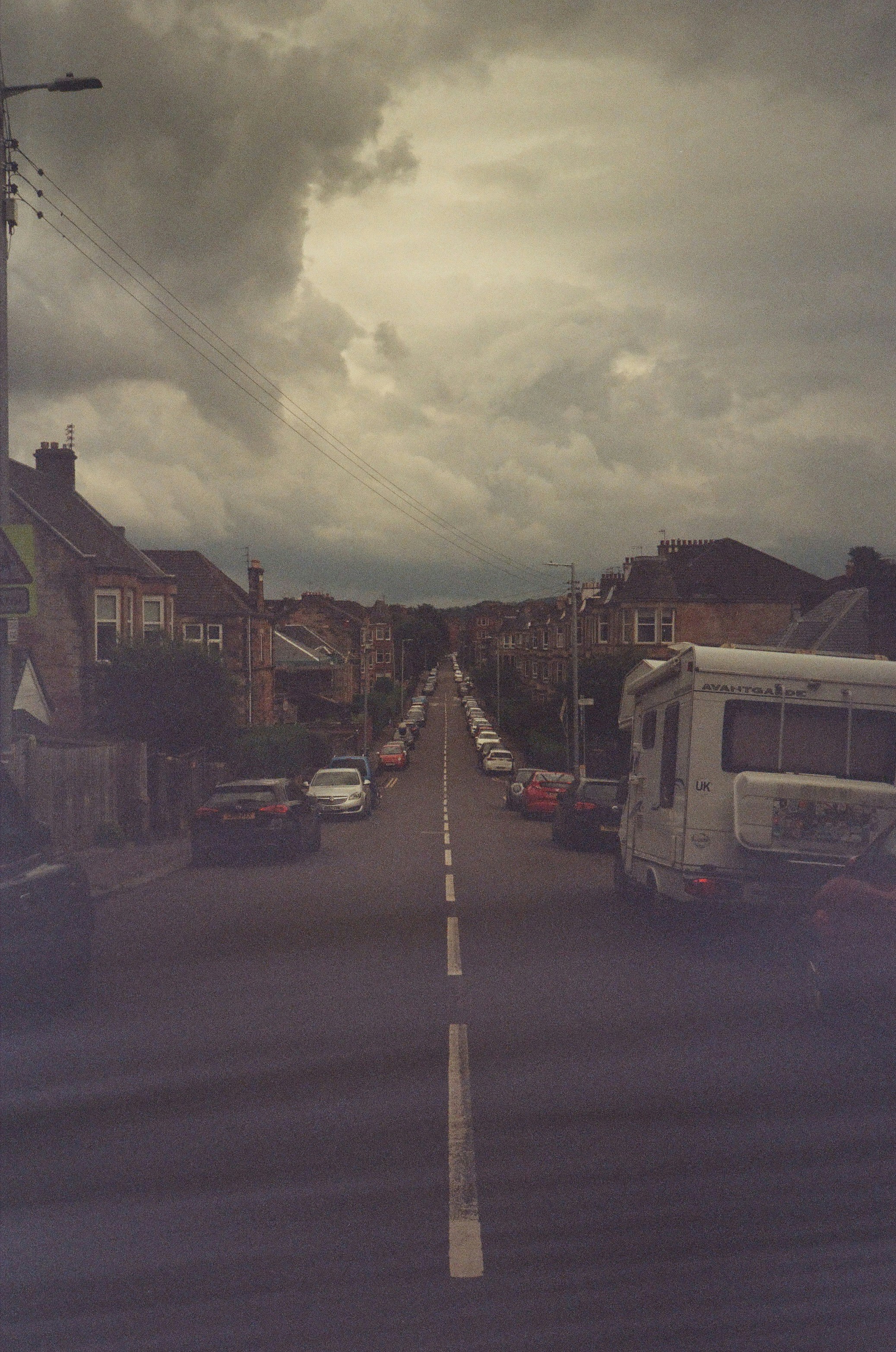 Street lined with houses and parked cars under cloudy sky