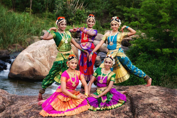 Five dancers in colourful traditional costumes posing outdoors by a river