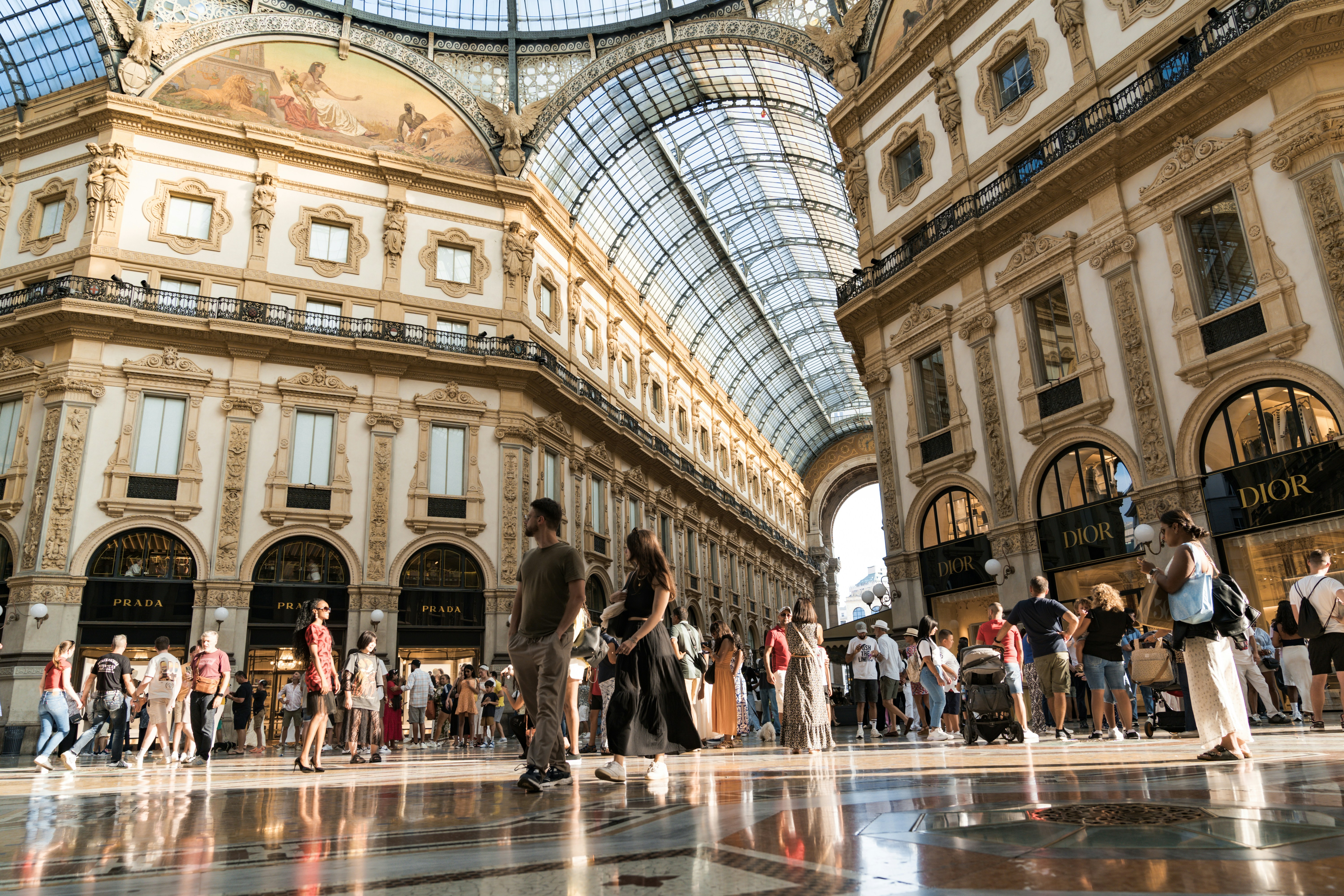 People walking inside a grand shopping arcade with glass ceiling.