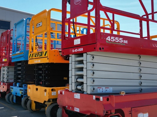Several colorful scissor lifts parked in a row.