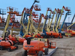 Multiple boom lifts parked in an outdoor lot.