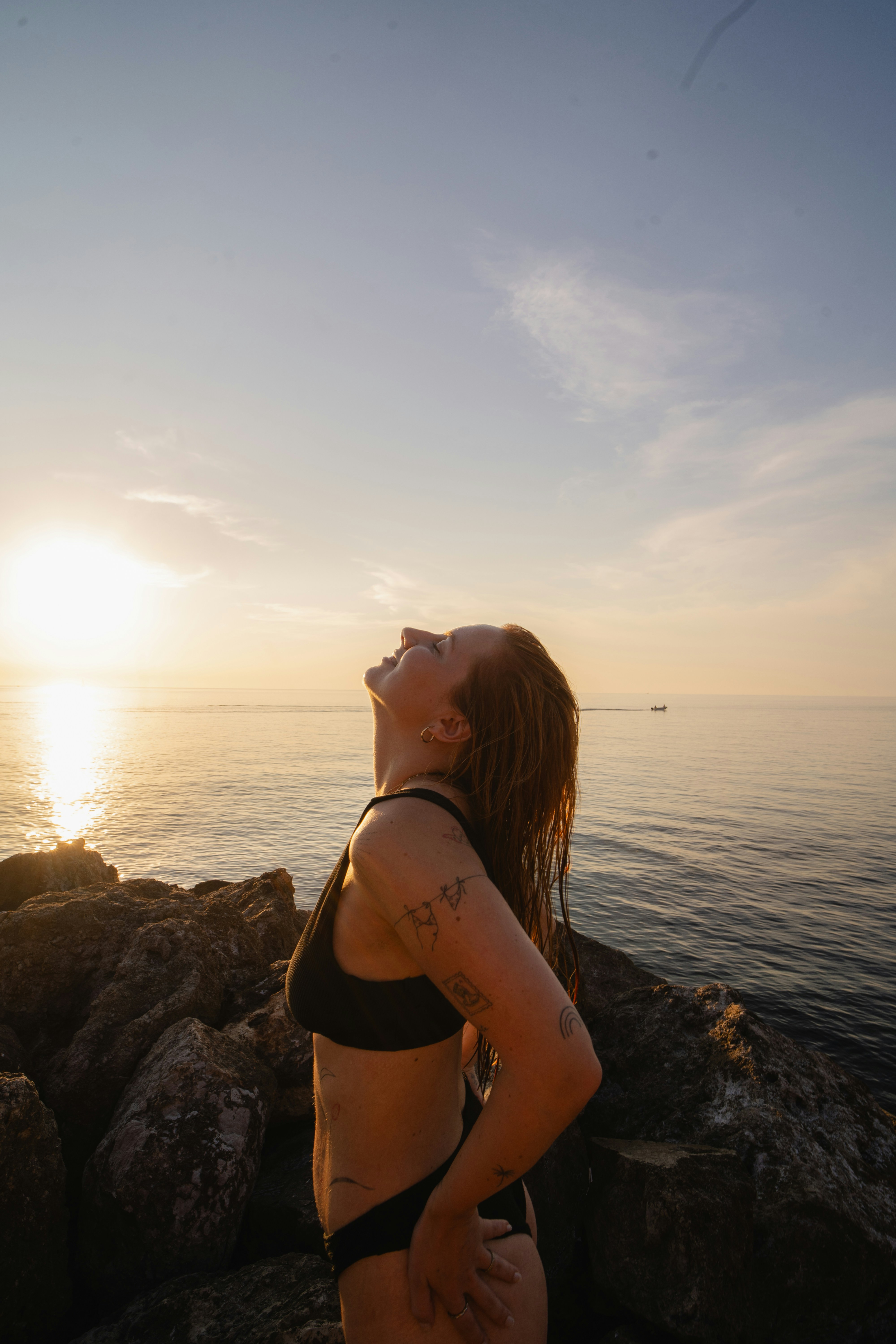 Donna in bikini che guarda il tramonto in riva al mare