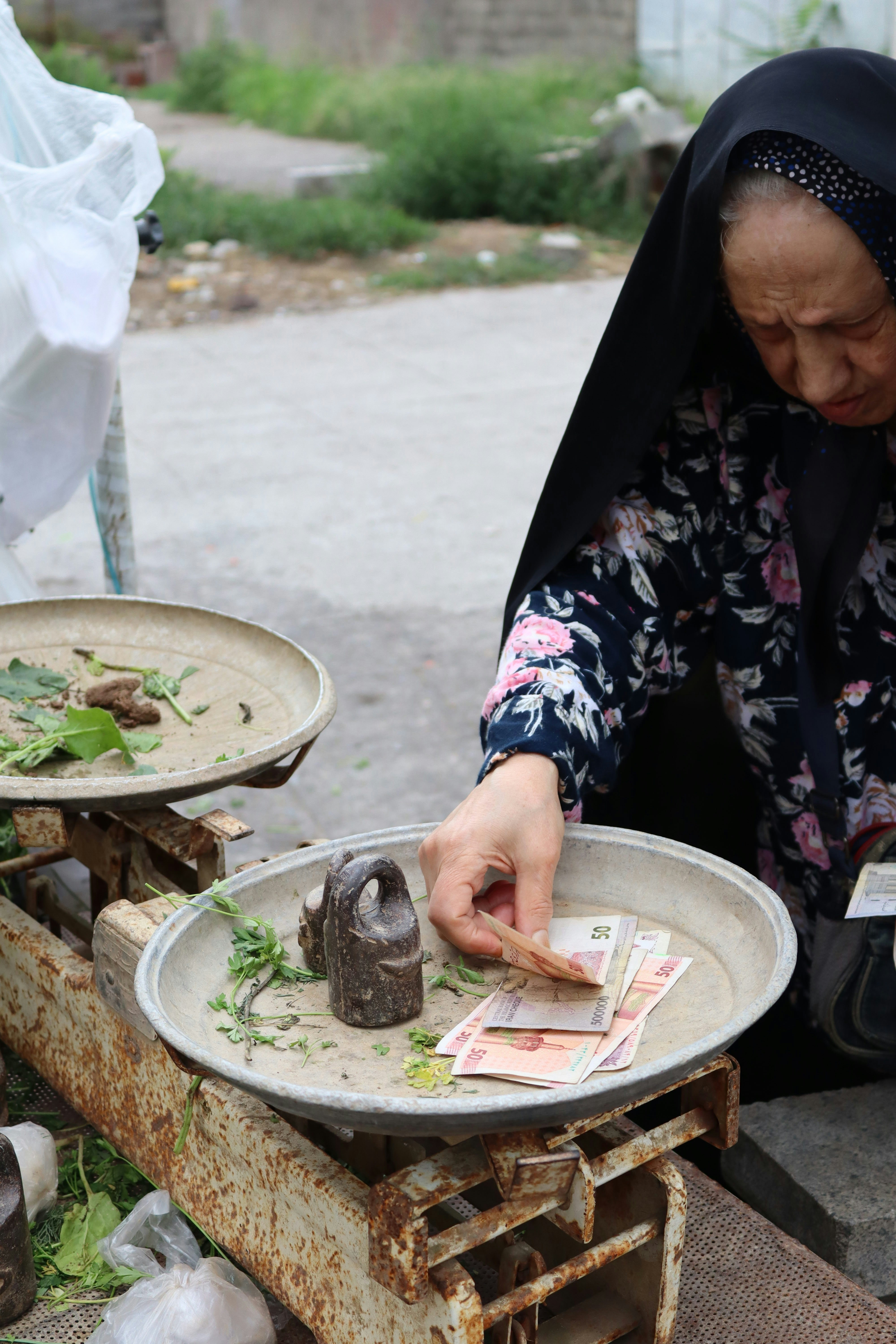 Elderly woman counts money at a market scale.