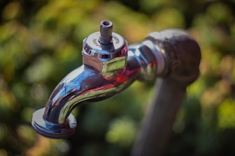 A shiny chrome faucet outdoors with blurred greenery.