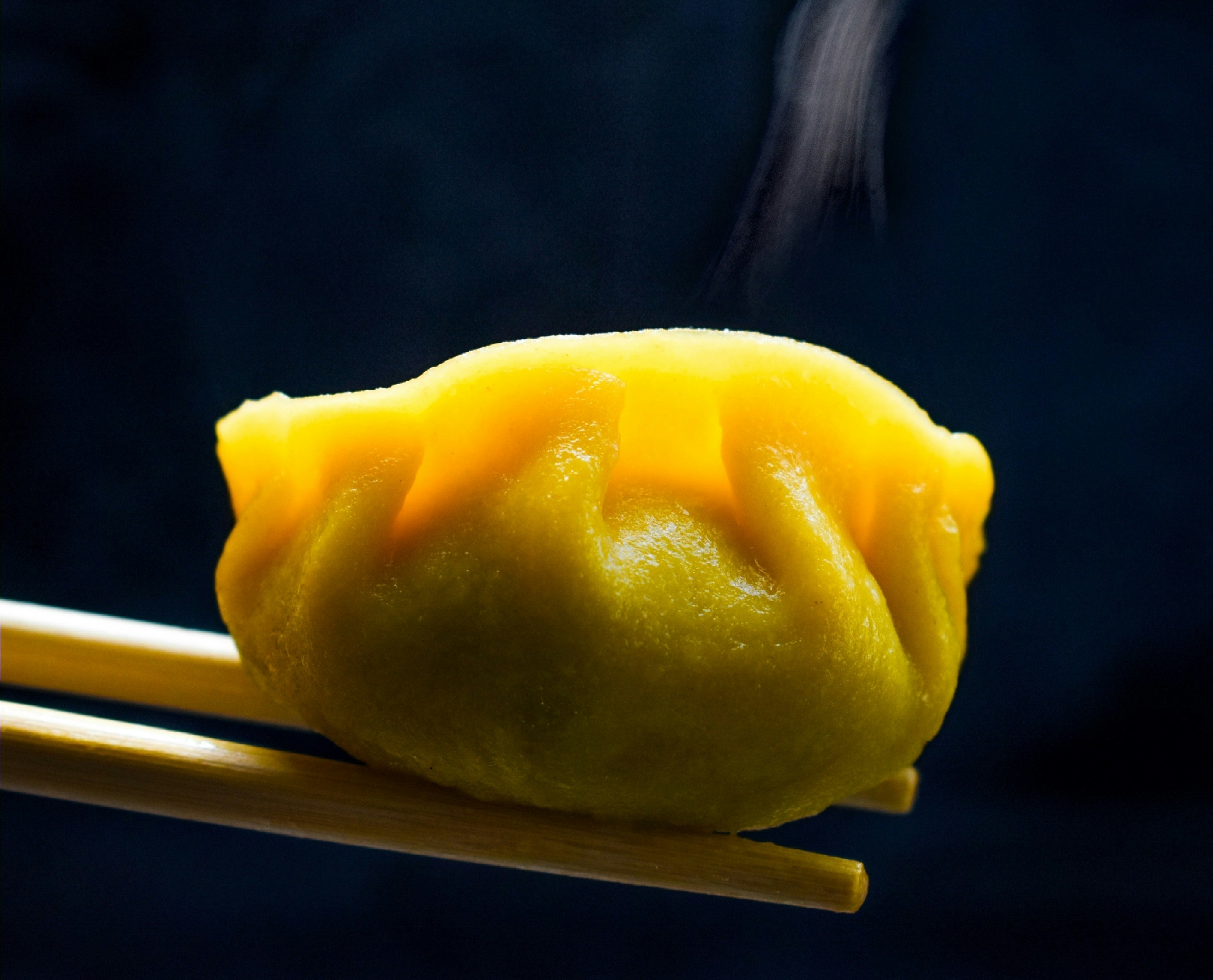 Single yellow dumpling held by chopsticks