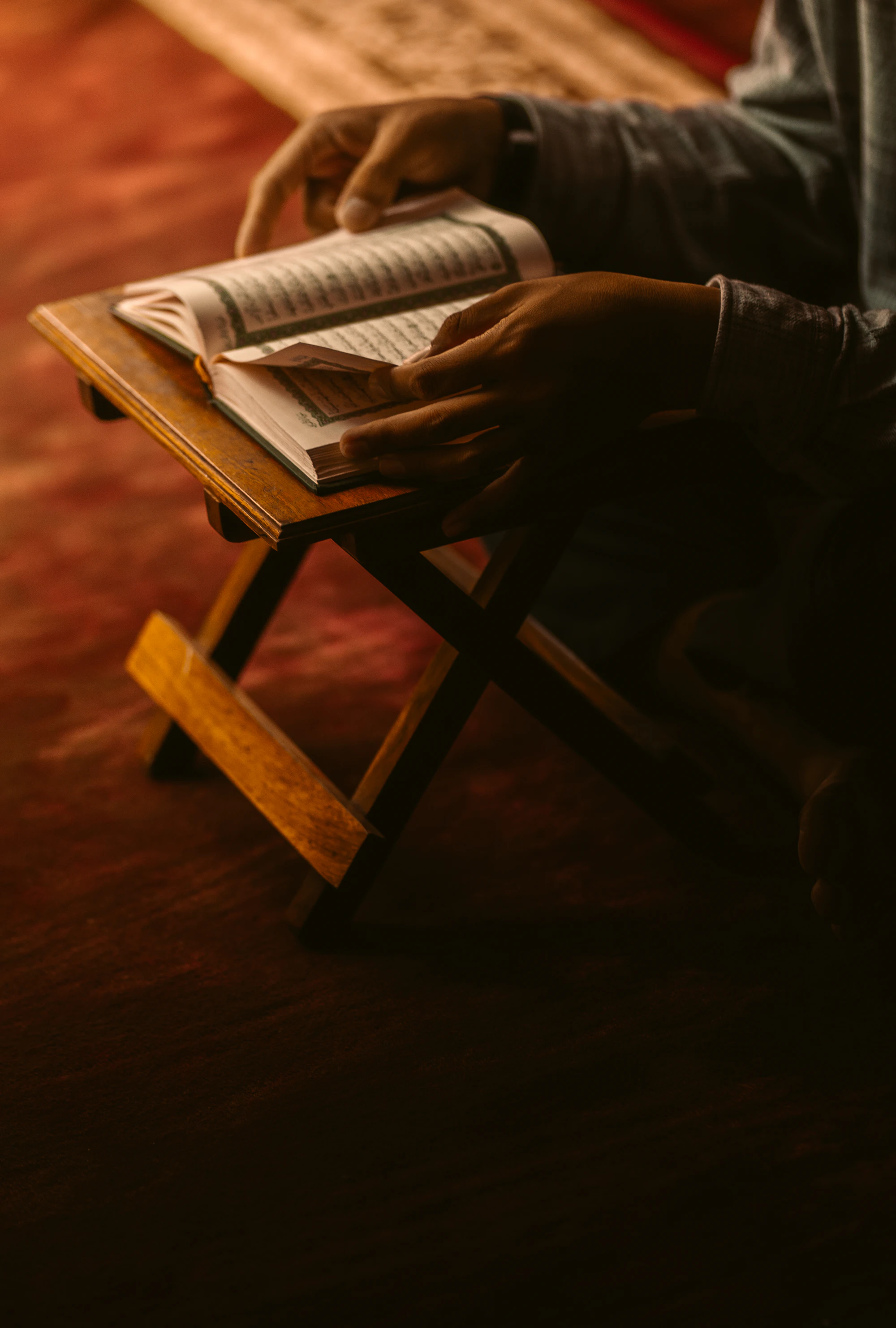 An open Quran resting on a carved wooden stand in warm light
