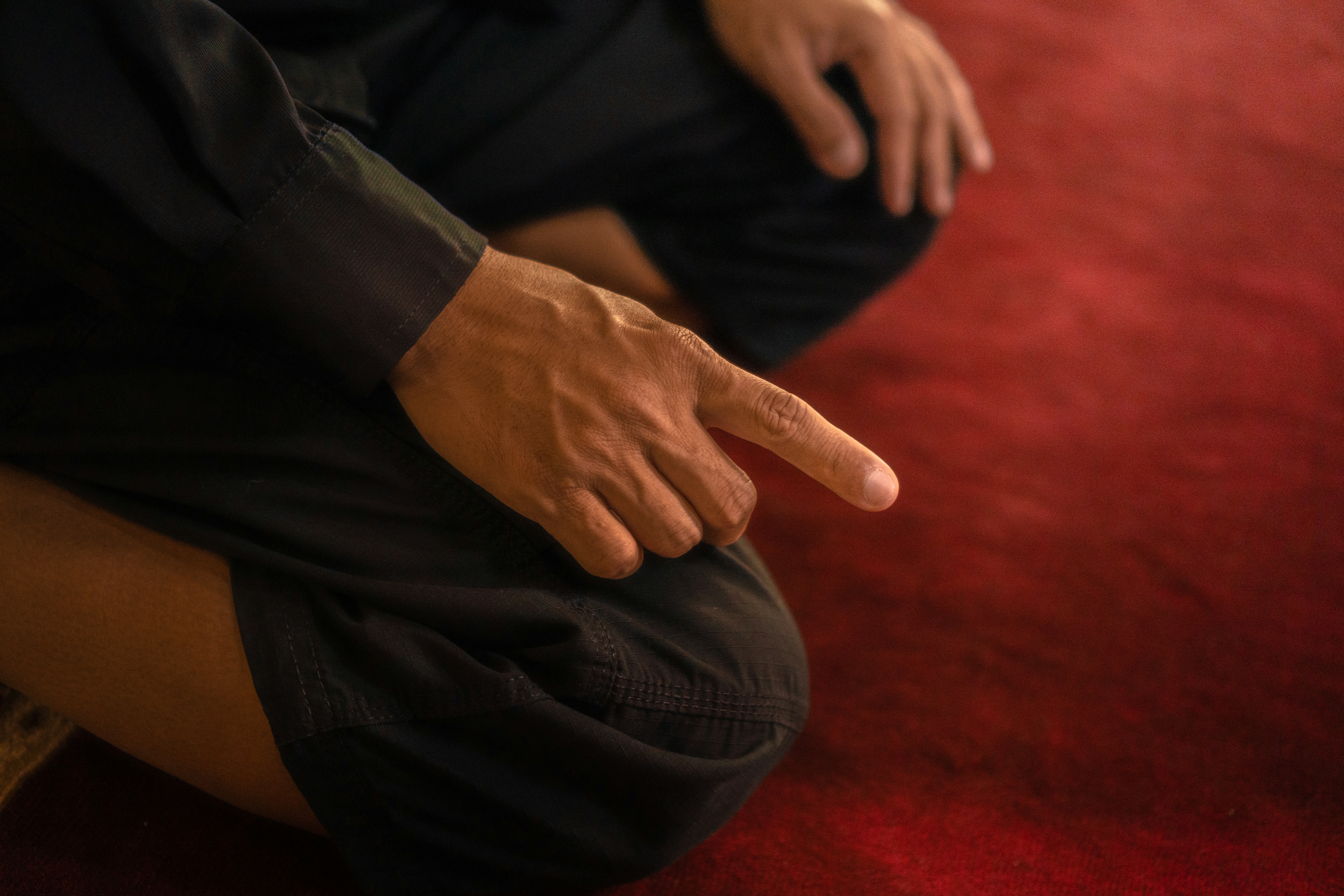 Un homme en prière pointe du doigt sur le tapis rouge.