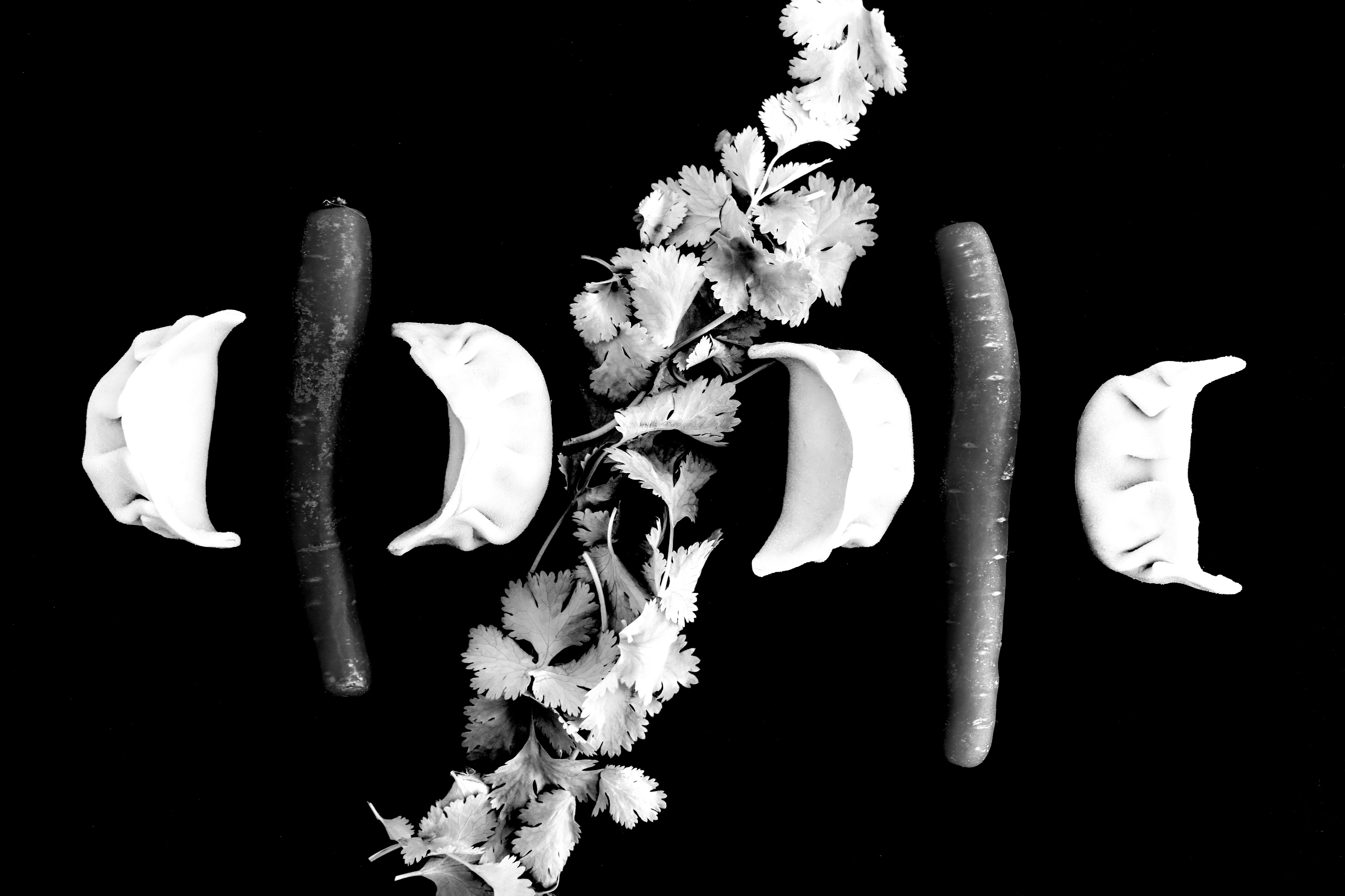 A black and white still life with dumplings, carrots and parsley