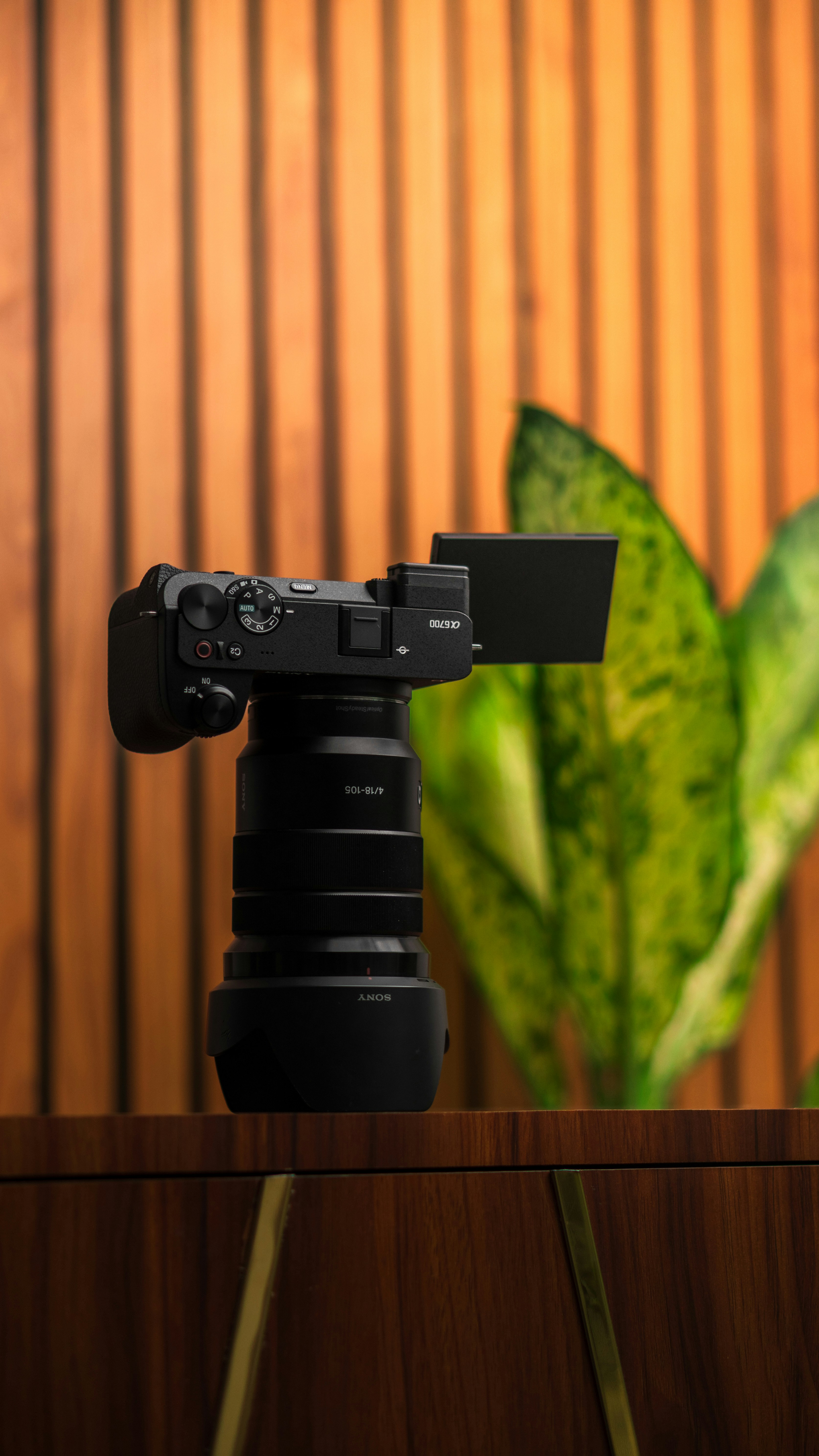 Câmera preta com lente na superfície de madeira, fundo ripado.